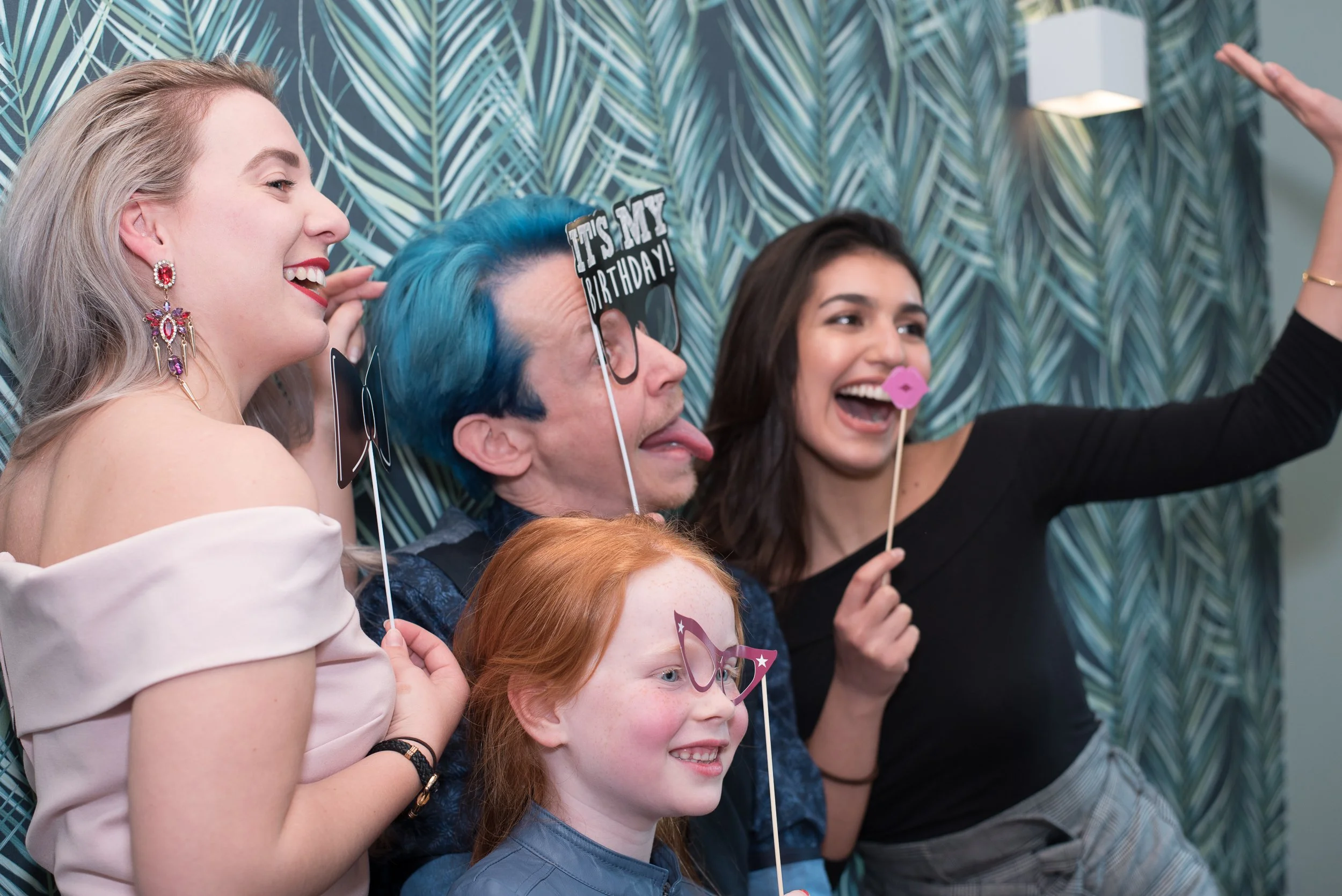 Vrolijke groepsfoto van volwassenen en een kind met fotobooth props tijdens een evenement.