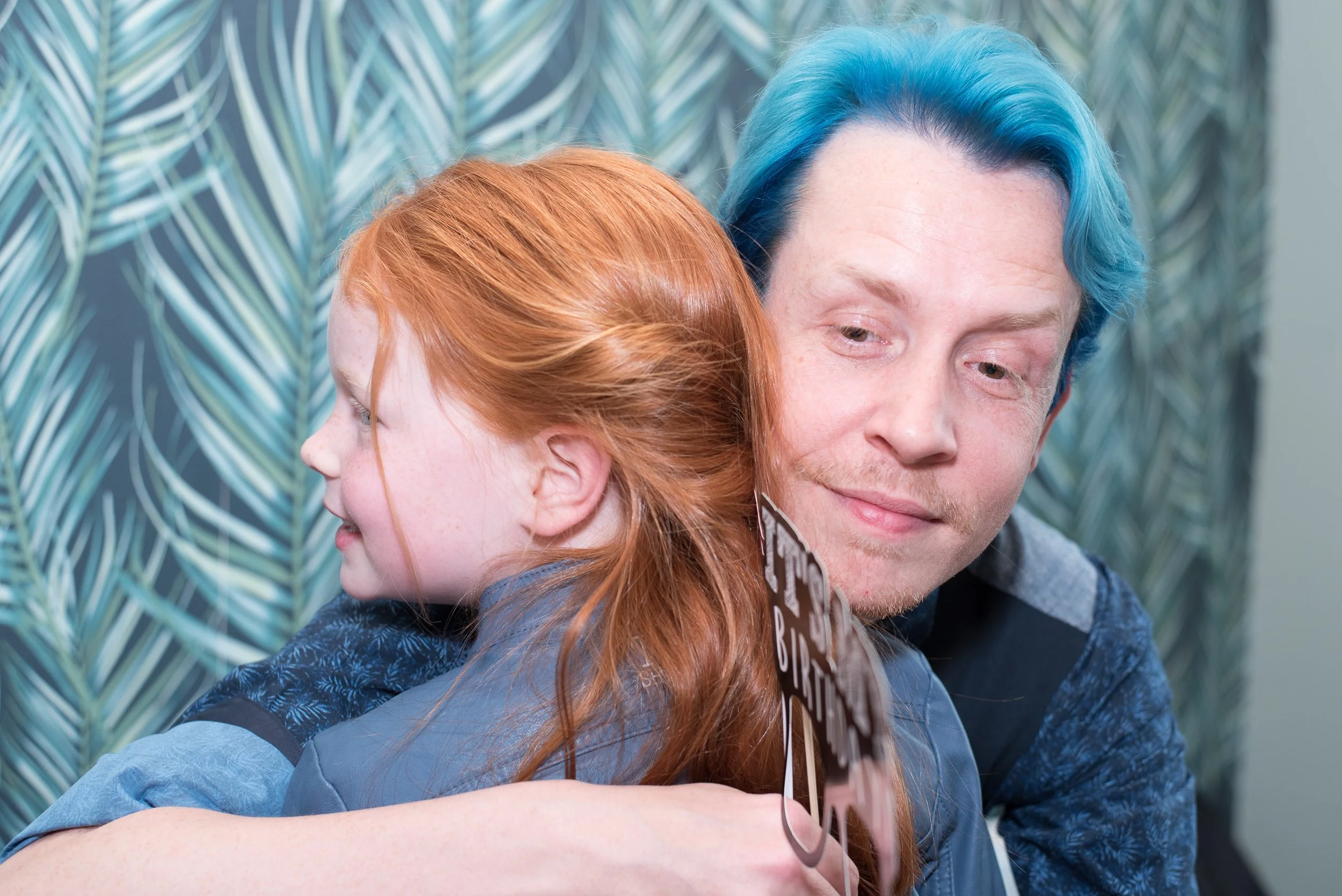 Intiem moment op een evenement: een man met blauw haar knuffelt een meisje met rood haar.