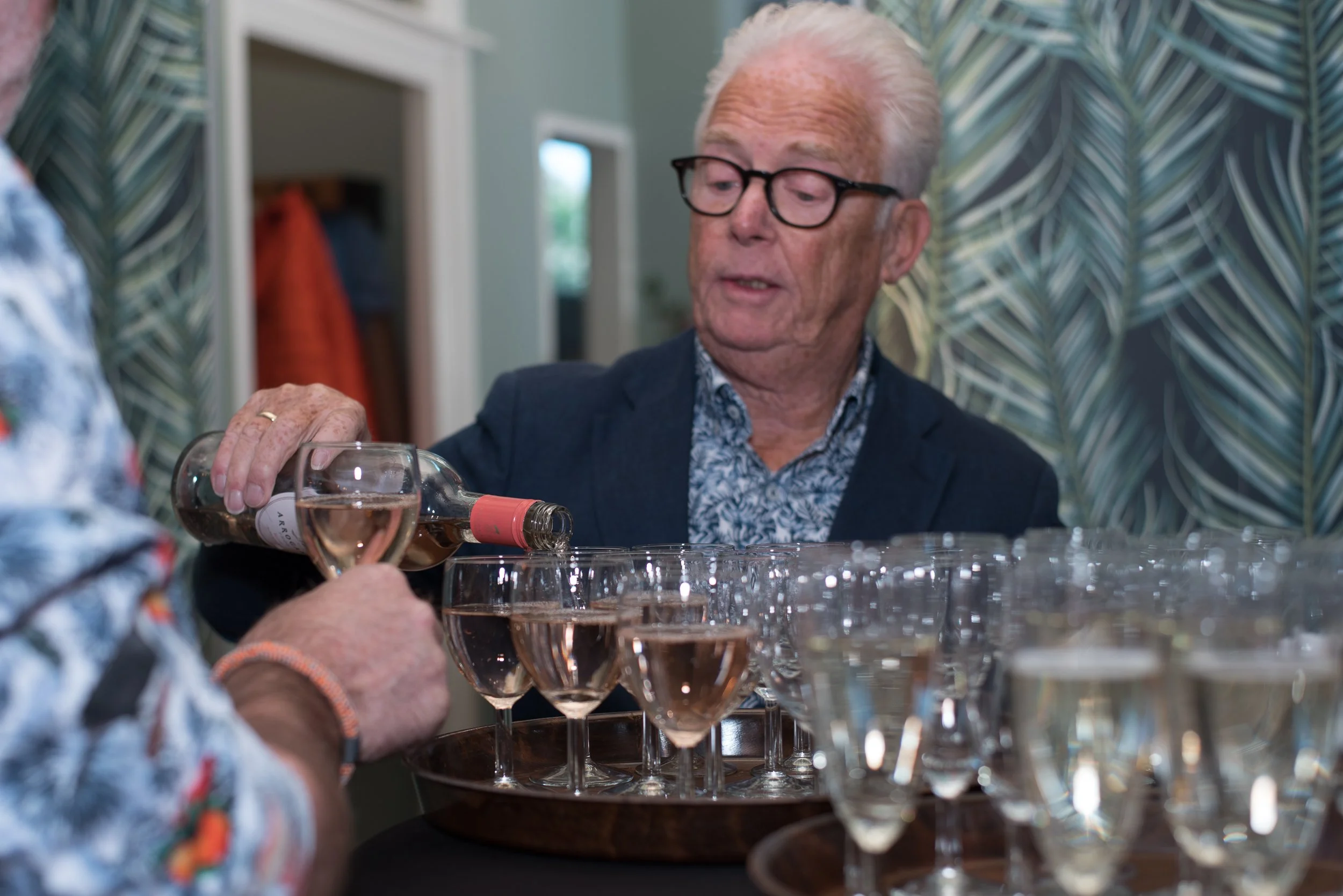 Professionele eventfotografie van een man met bril die glazen witte wijn inschenkt.