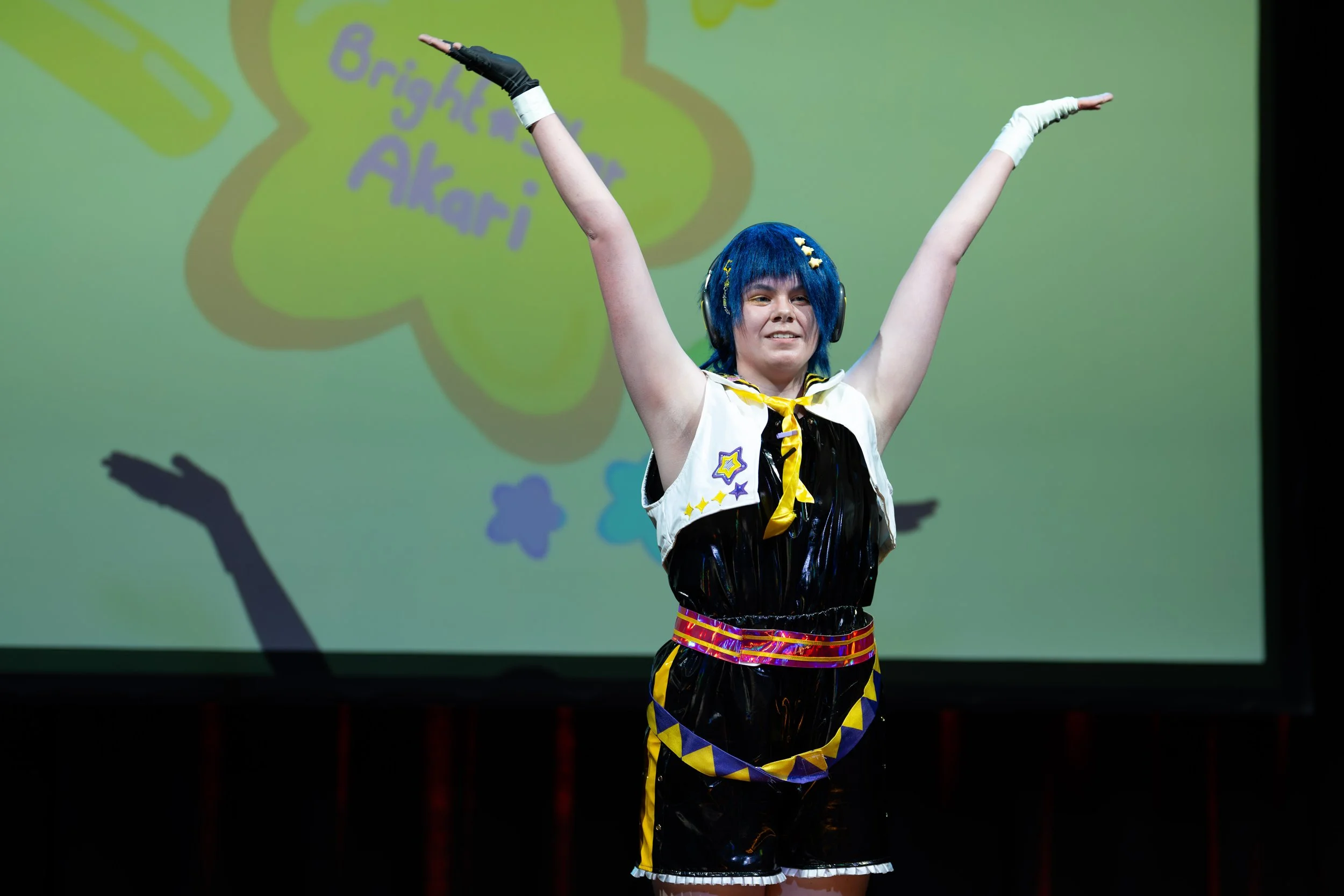 Podiumfotografie van een artiest met blauw haar en de armen omhoog tijdens een energieke show.