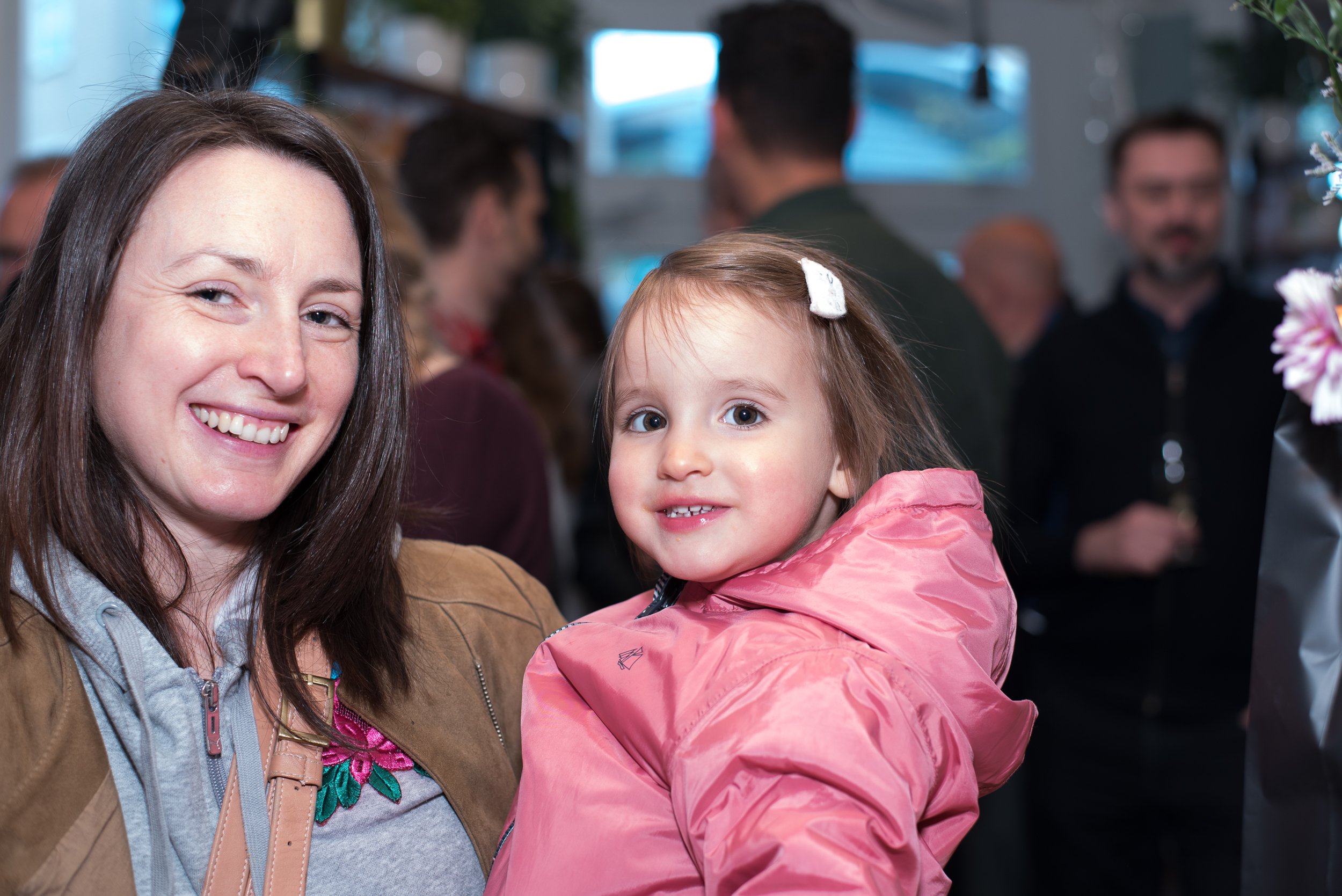 Sfeervol portret van een moeder met haar kind in een roze jasje tijdens een evenement.