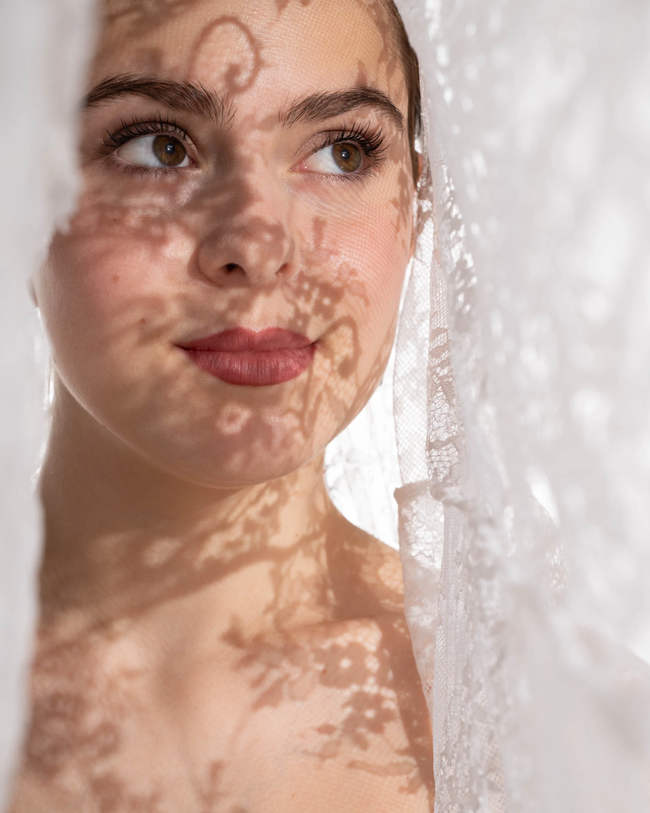 Artistiek portret van een jonge vrouw met een subtiel schaduwpatroon van kant op haar gezicht.