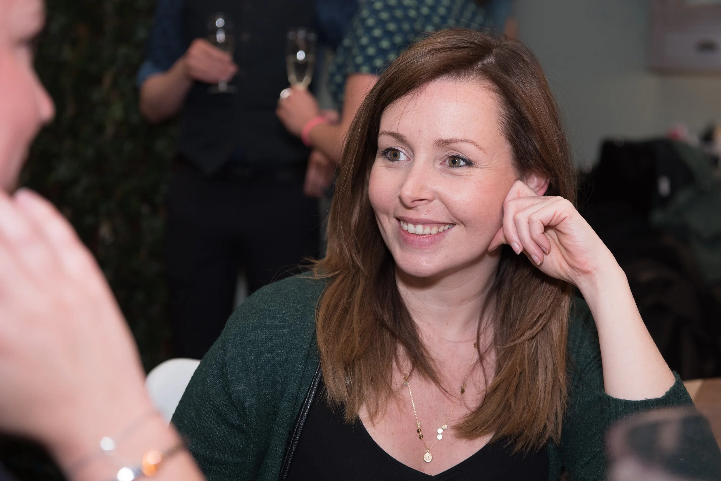 Portret van een vrouw in een groene trui die luistert tijdens een presentatie of congres.
