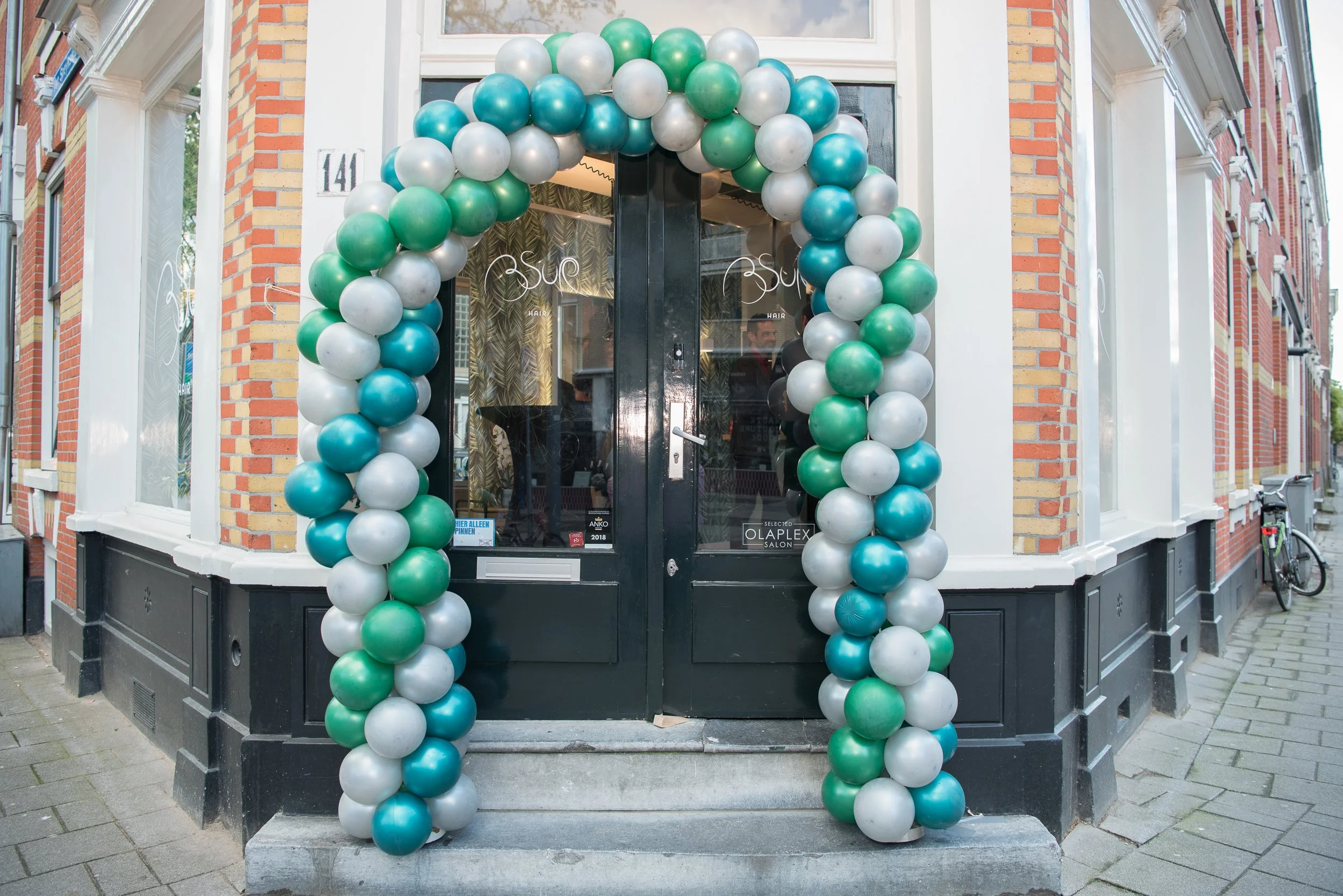 Sfeerbeeld van een evenementenlocatie met een feestelijke boog van groene en witte ballonnen bij de ingang.
