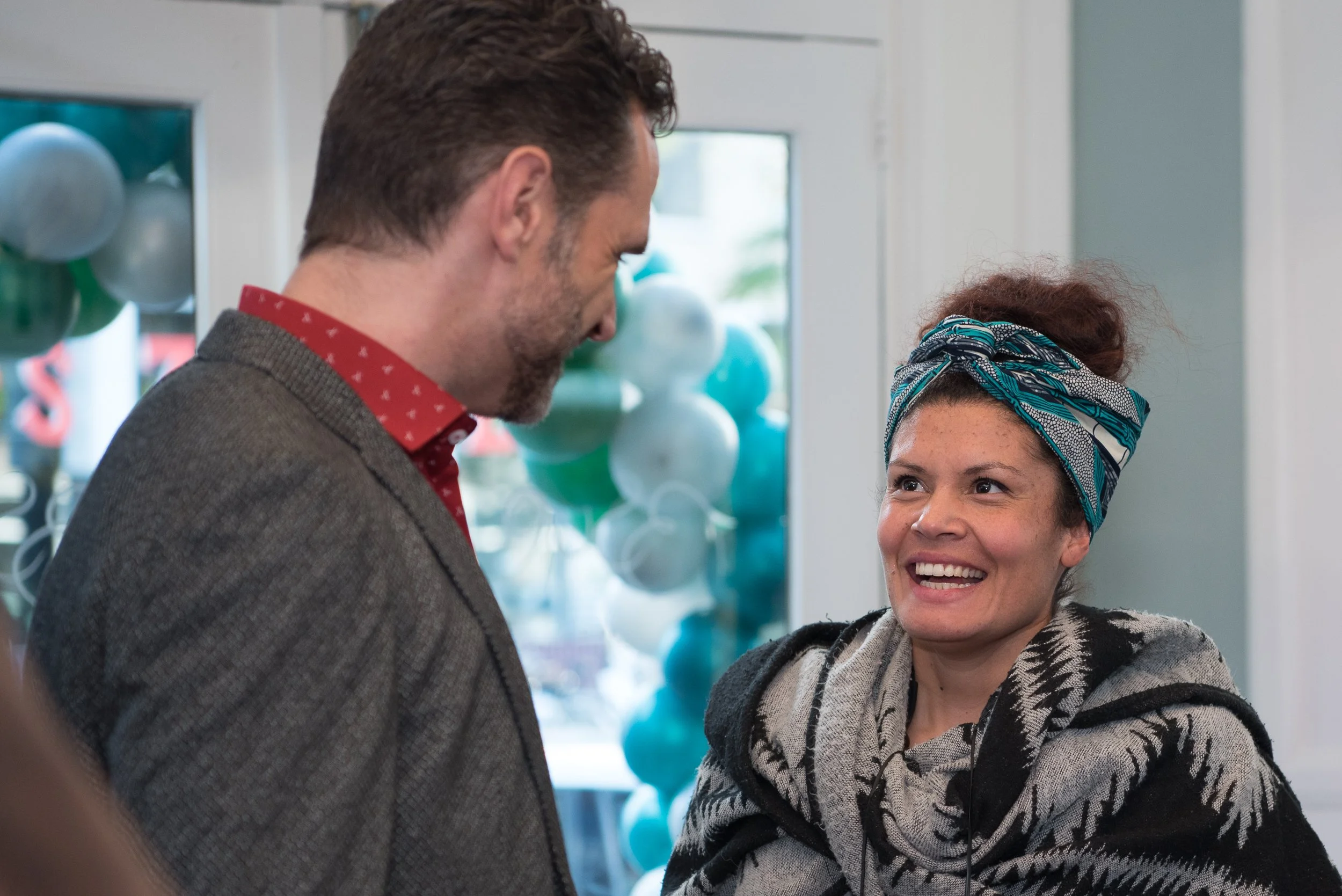 Spontane eventfotografie van een man en vrouw in gesprek met een groen-witte ballonnenboog op de achtergrond.