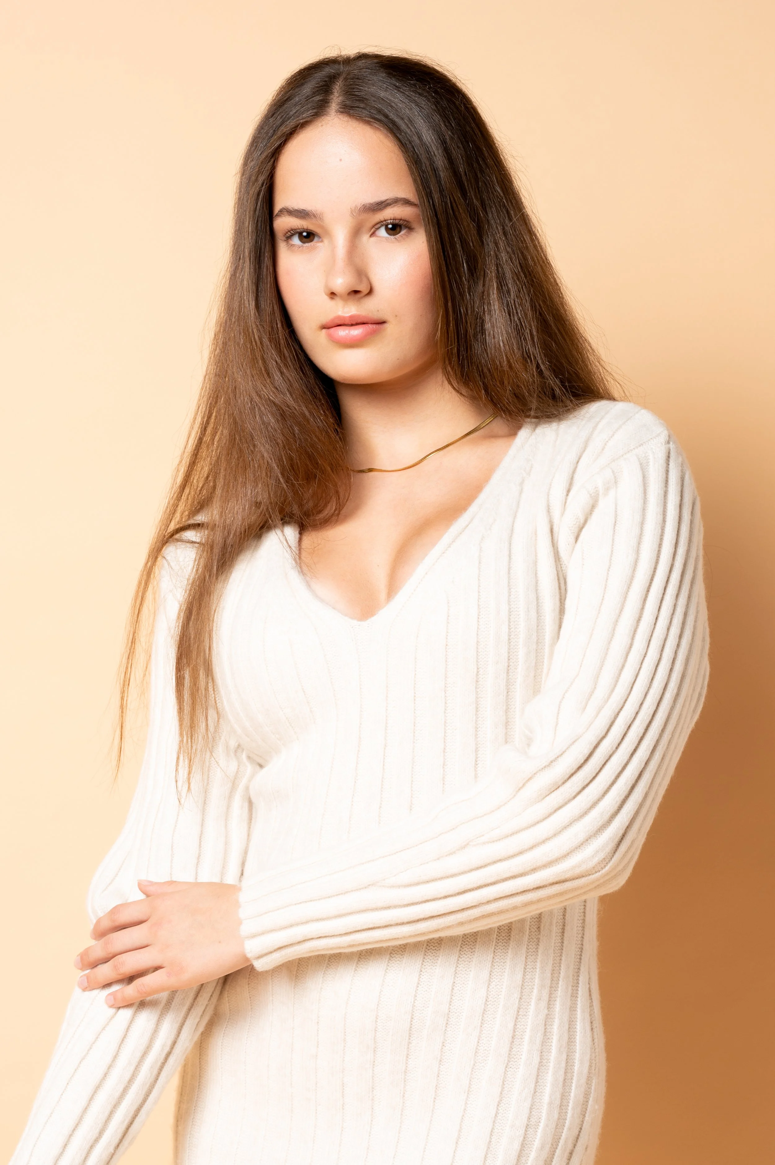 Studio headshot van een jonge vrouw met lang haar in een gebreide witte trui.