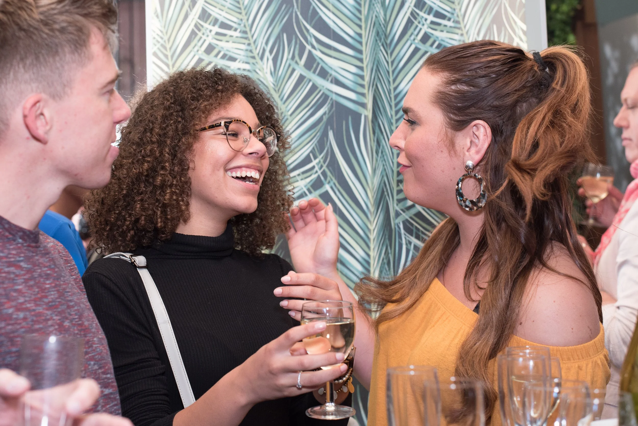 Sfeerimpressie van twee lachende vrouwen in gesprek met een glas wijn tijdens een netwerkborrel.