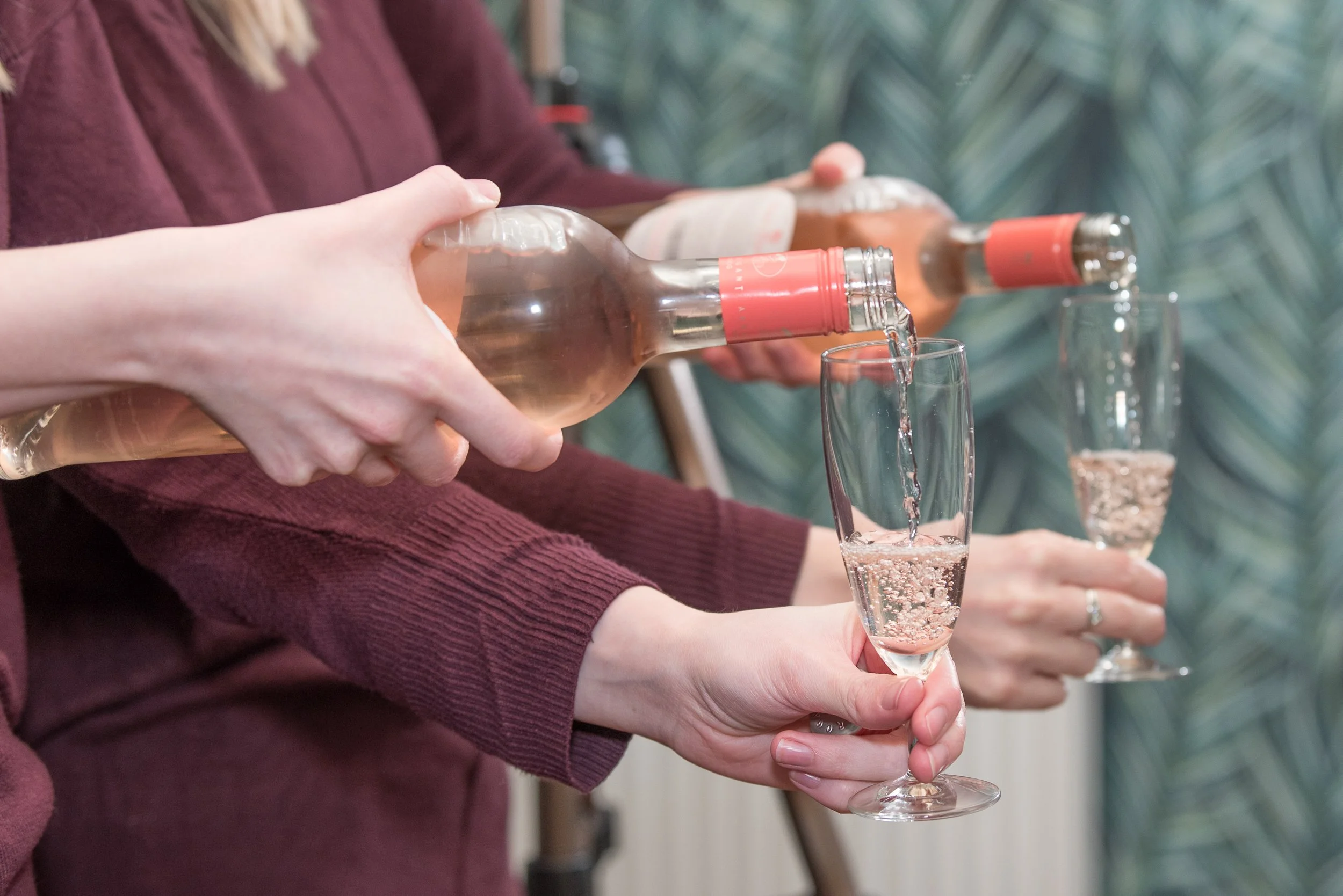 Detailopname van handen die roséwijn inschenken tijdens een borrel of zakelijk evenement.