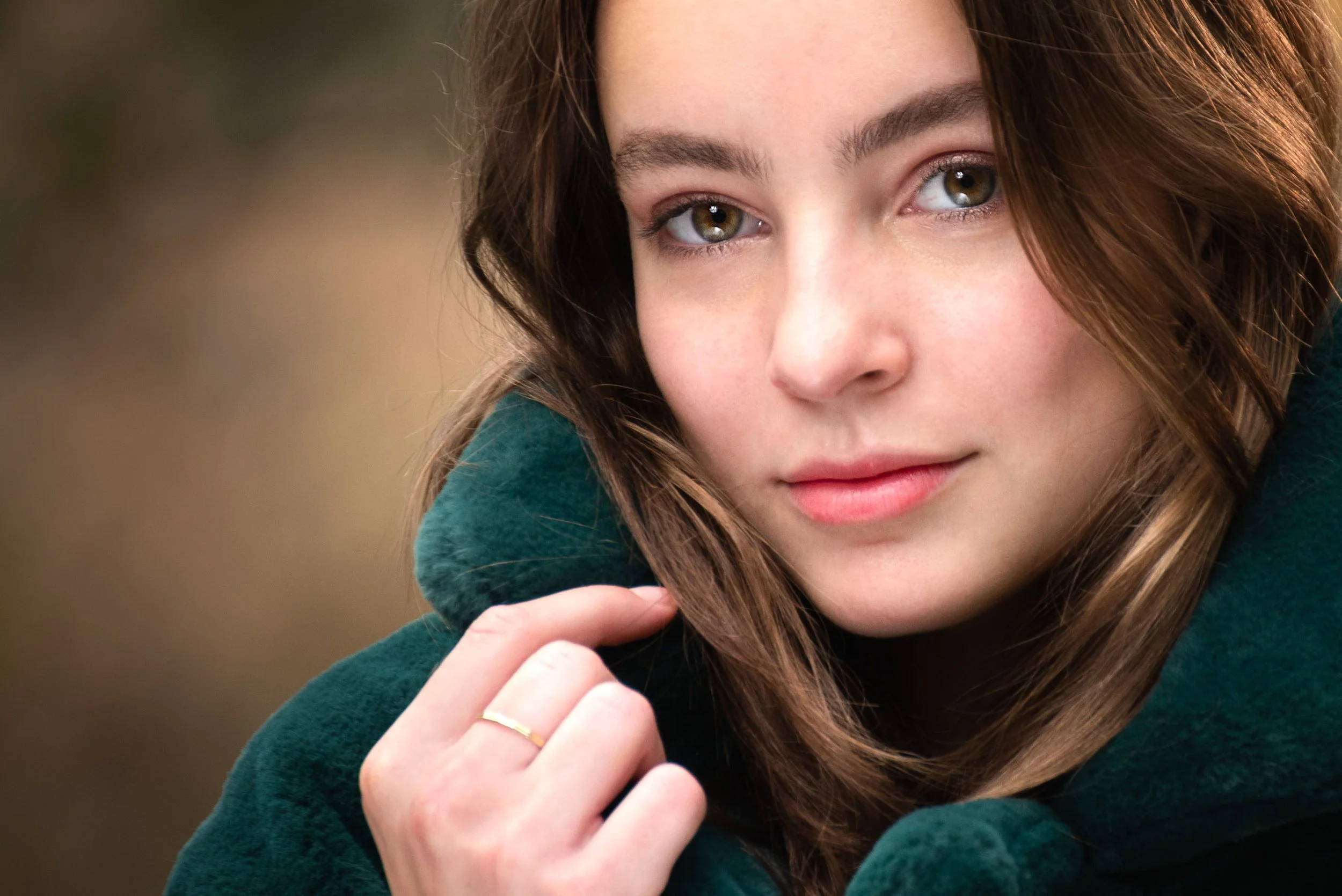 Sfeervol portret van een jonge vrouw met een opgetrokken groene bontkraag in de natuur.