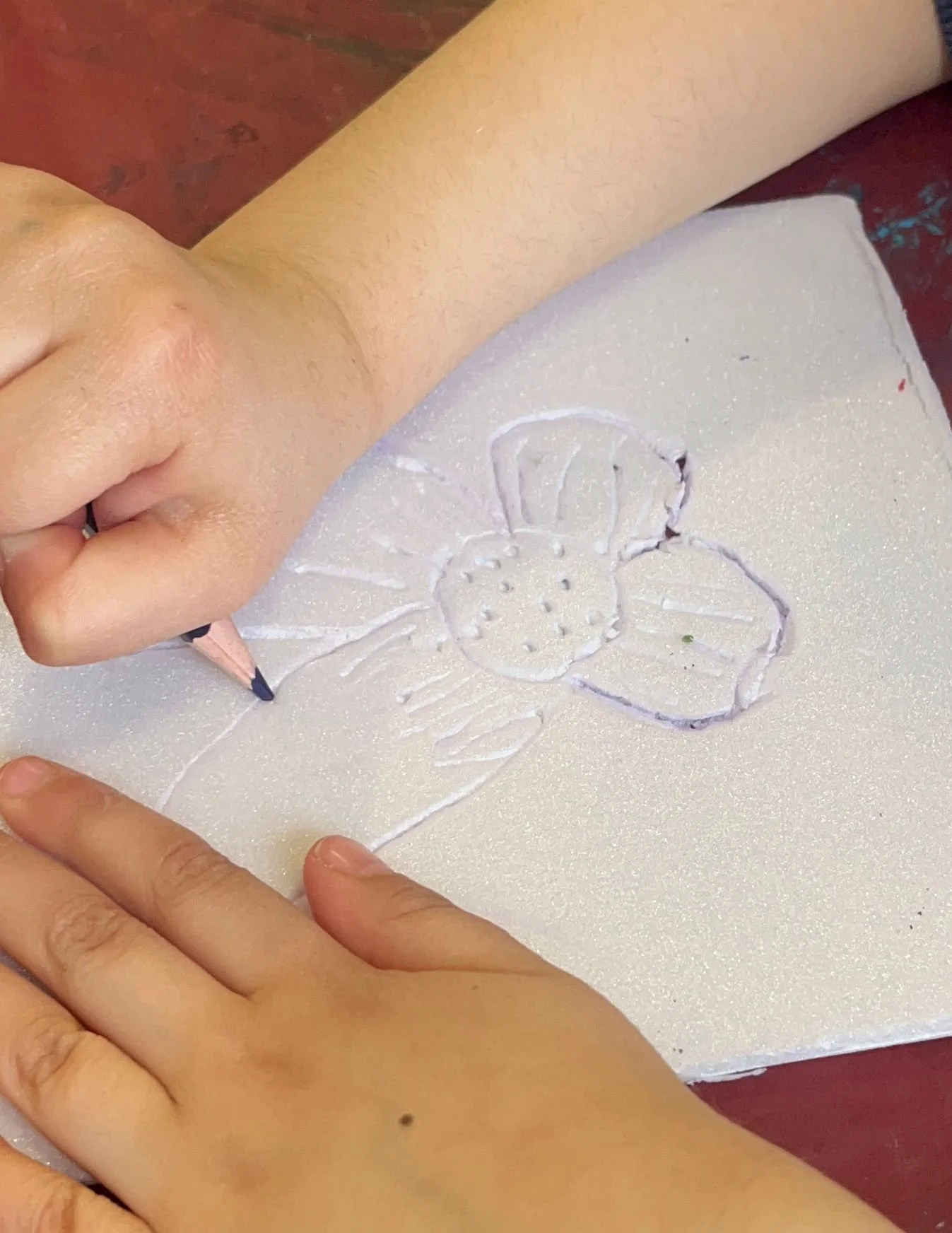 A person is drawing a butterfly on a piece of white paper with a pink colored pencil.