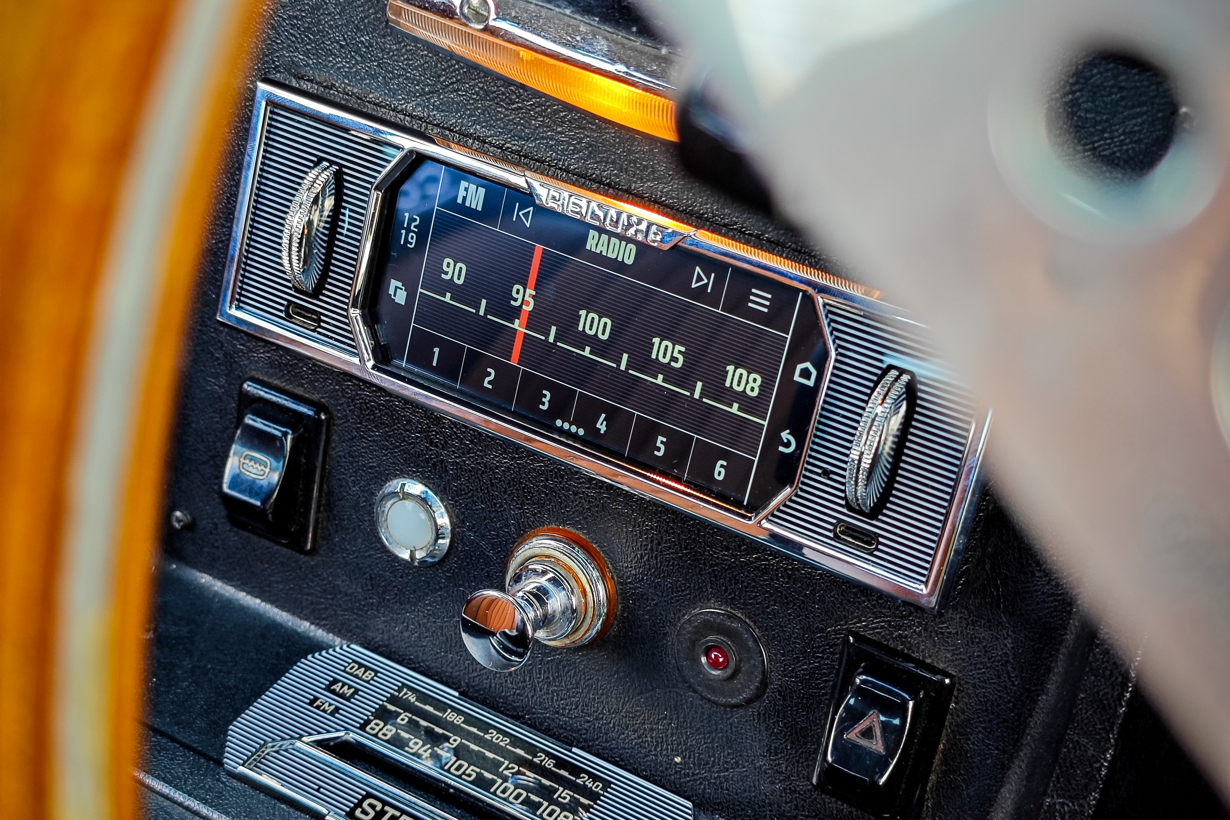 Close-up of a vintage car dashboard featuring a radio with a blue display, rotary controls, and various knobs.