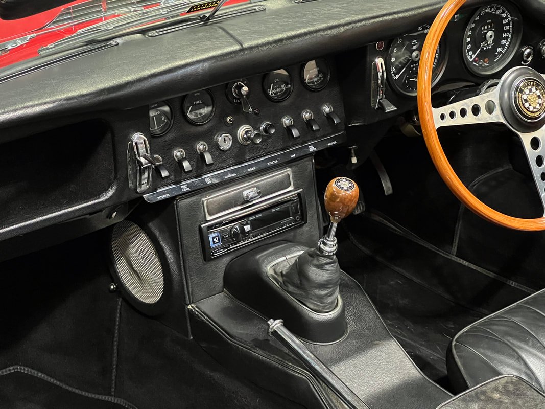 Interior of a Jaguar E-Type with a black plastic 90s radio, with very limited function and does not match the beautiful design of this Jag.