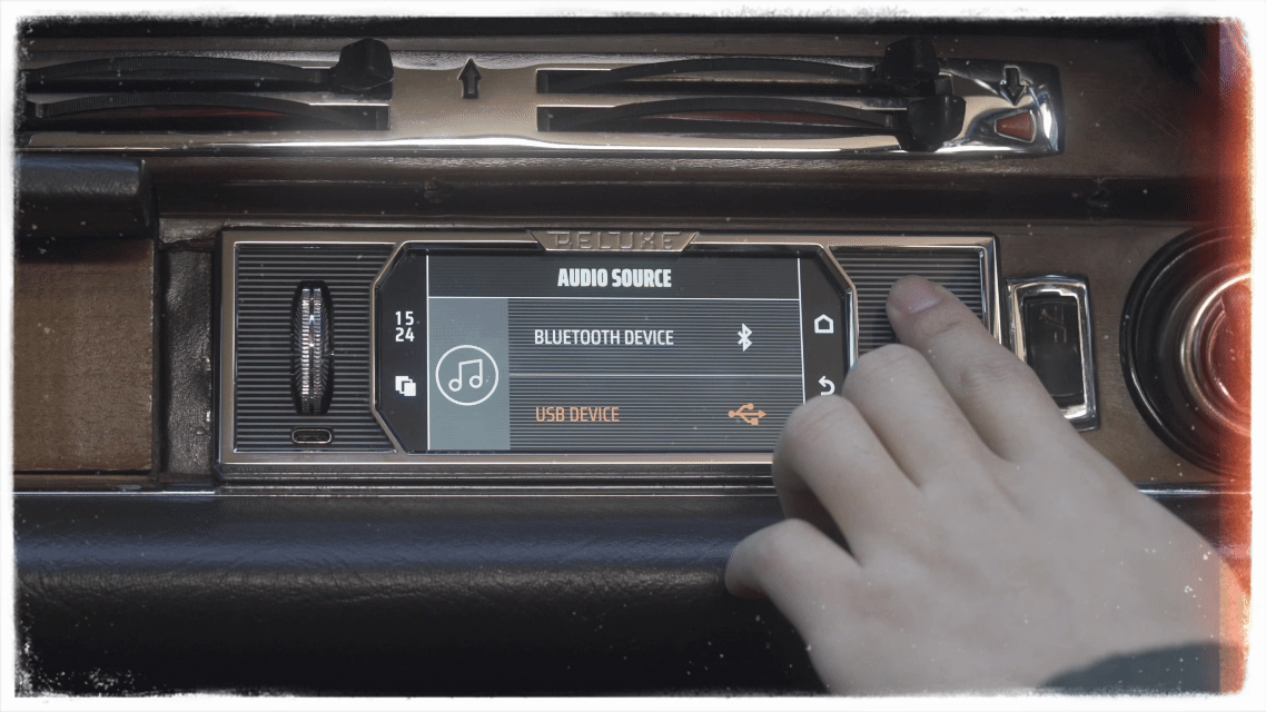 Car stereo display showing audio sources: Bluetooth device, USB device, and a music note icon, with a person's hand interacting with the screen.