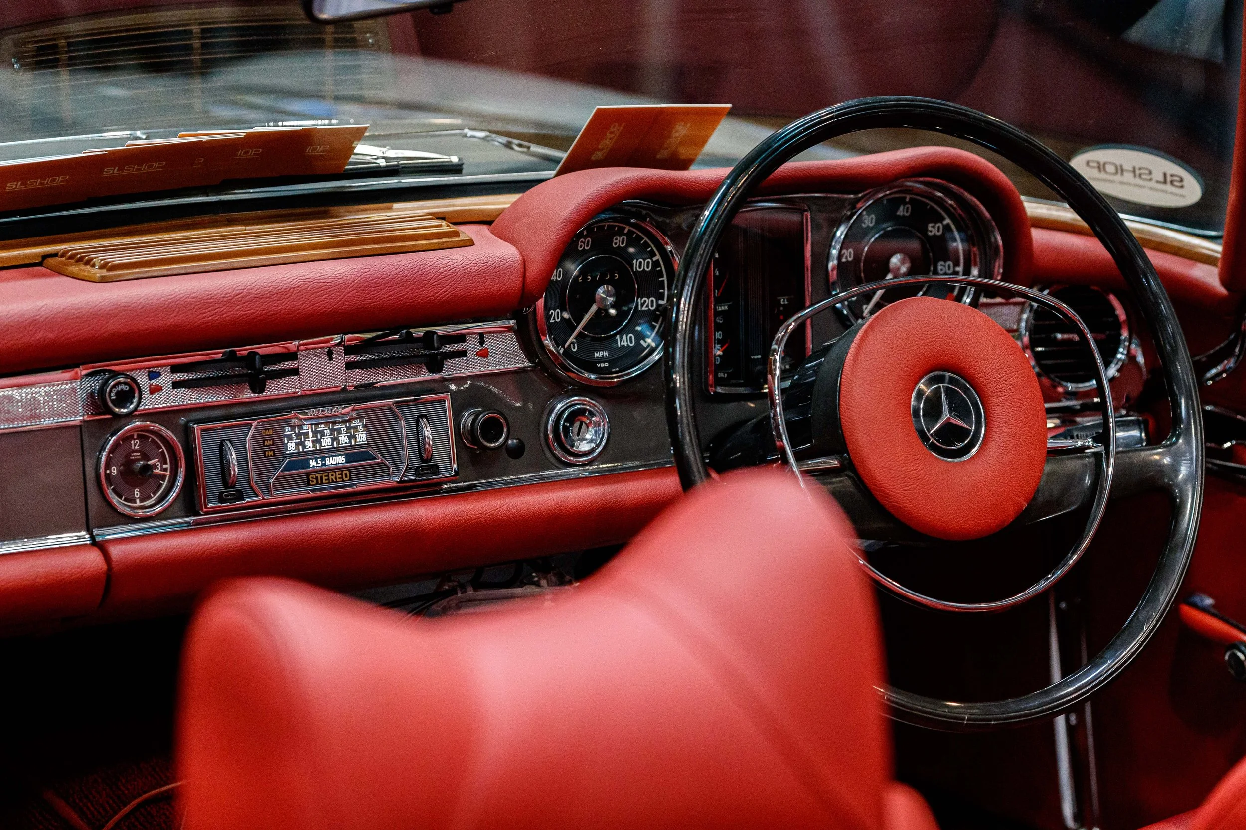 The interior of a vintage Mercedes-Benz car with a red dashboard, steering wheel with Mercedes logo, and analog gauges.