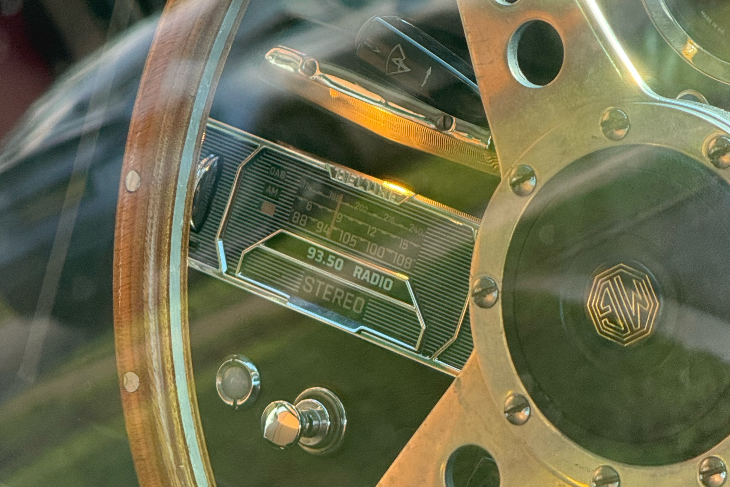 Close-up view of a vintage car steering wheel, radio, and dashboard with an analog radio displaying 93.50 FM Stereo.