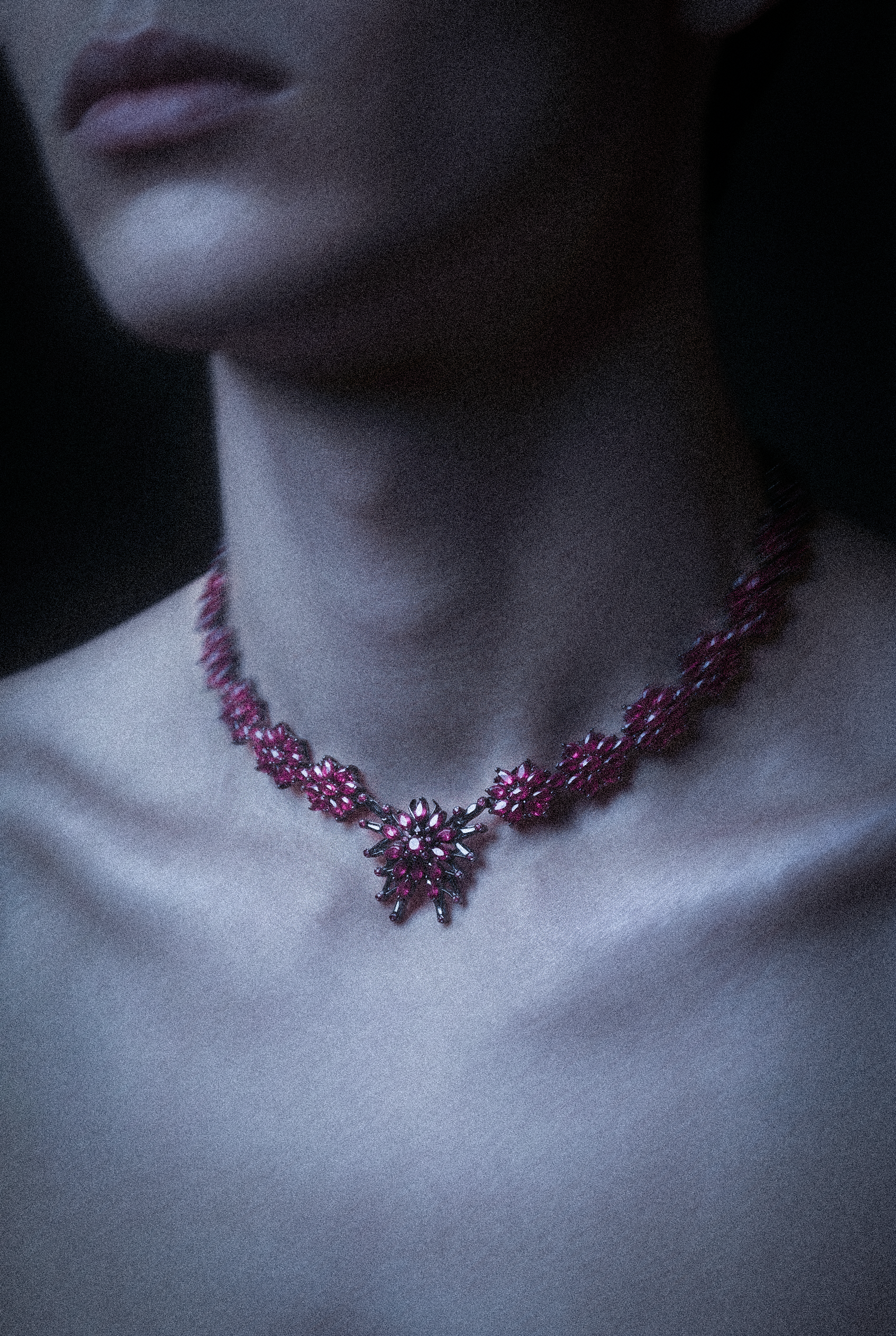 Close-up of a person wearing a pink gemstone necklace with a floral design, with visible lips and neck.