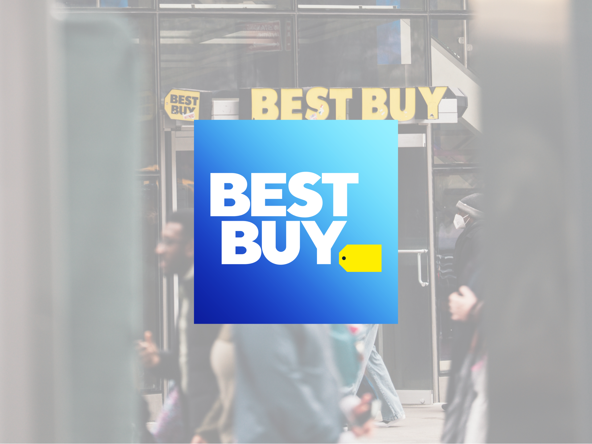 Close-up of a Best Buy storefront with the blue sign prominently displayed. Pedestrians are visible walking past the store, partially obscured by the photo's framing.
