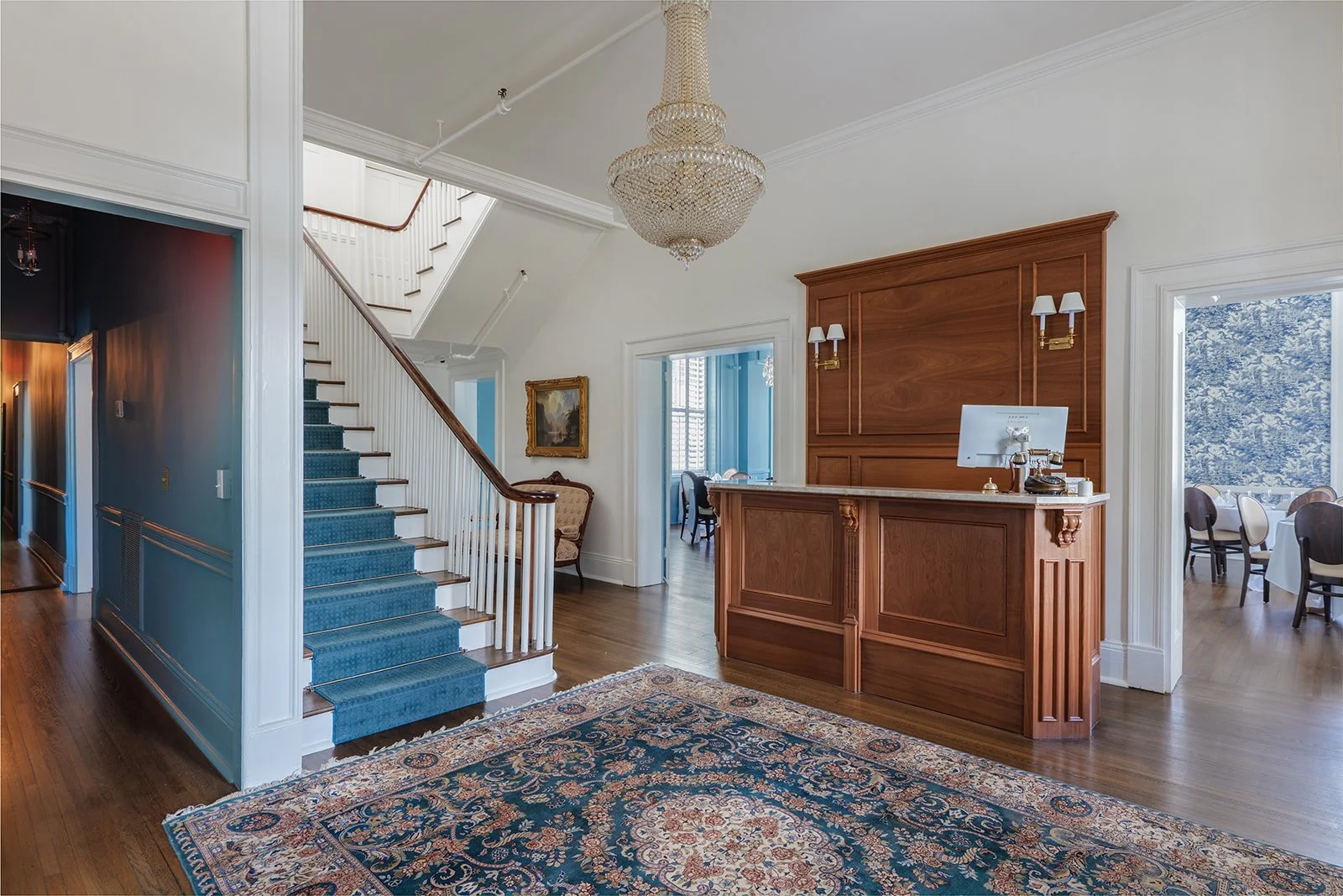 Hotel Everett | Boutique Hotel in Winnsboro, SC, historic hotel | Interior of a hotel lobby with a staircase, reception desk, chandelier, and a seating area visible in background.