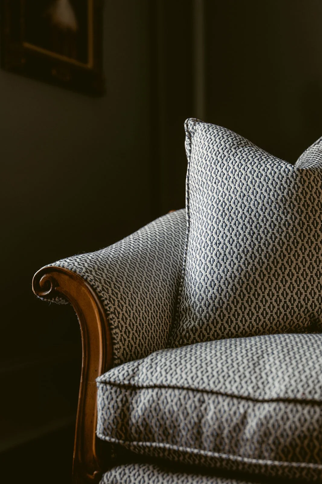 Close-up of patterned upholstered armchair with wood trim, set against a dark background.
