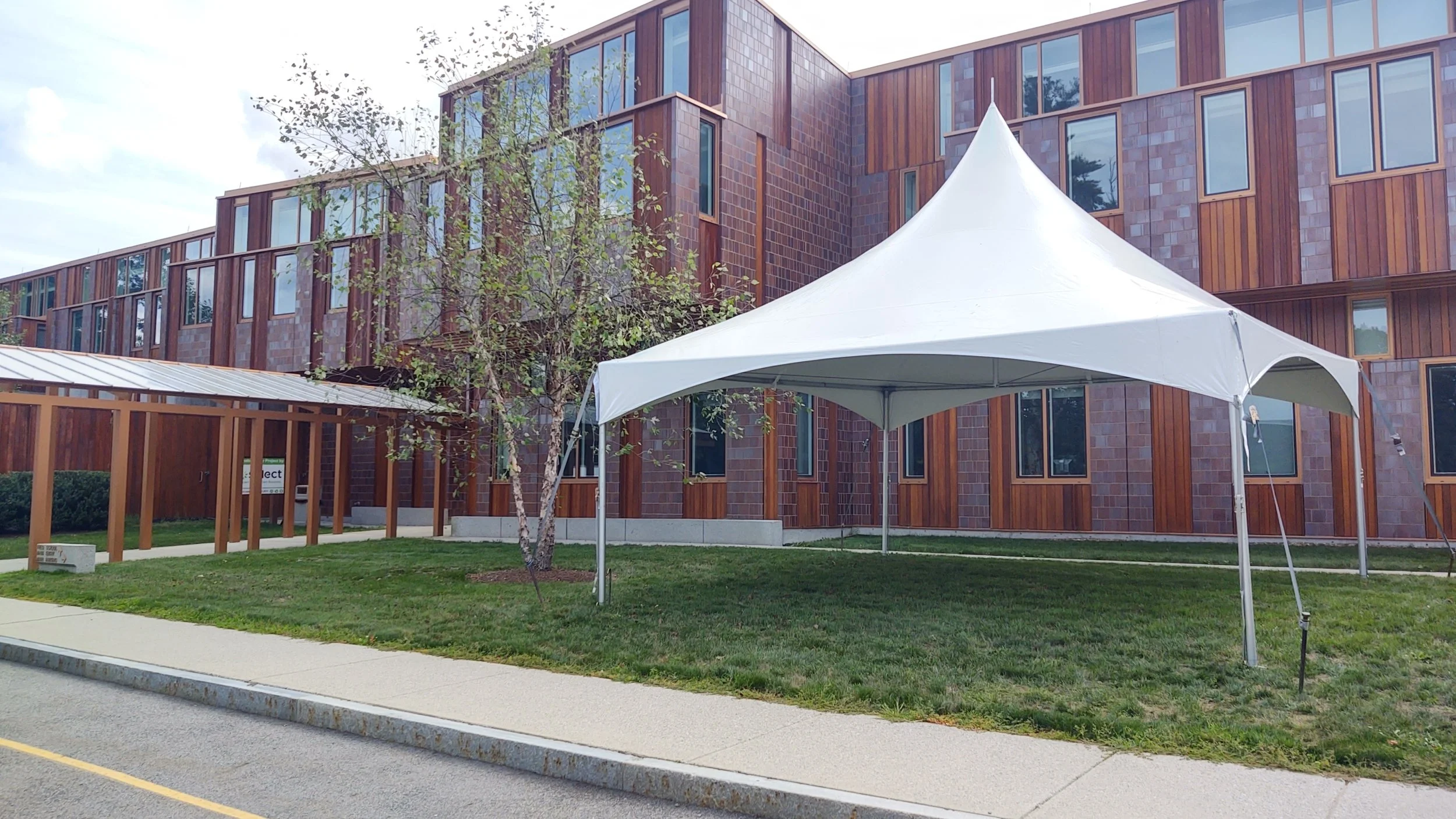 A white event tent set up on a grassy area in front of a multi-story brick and wood building.