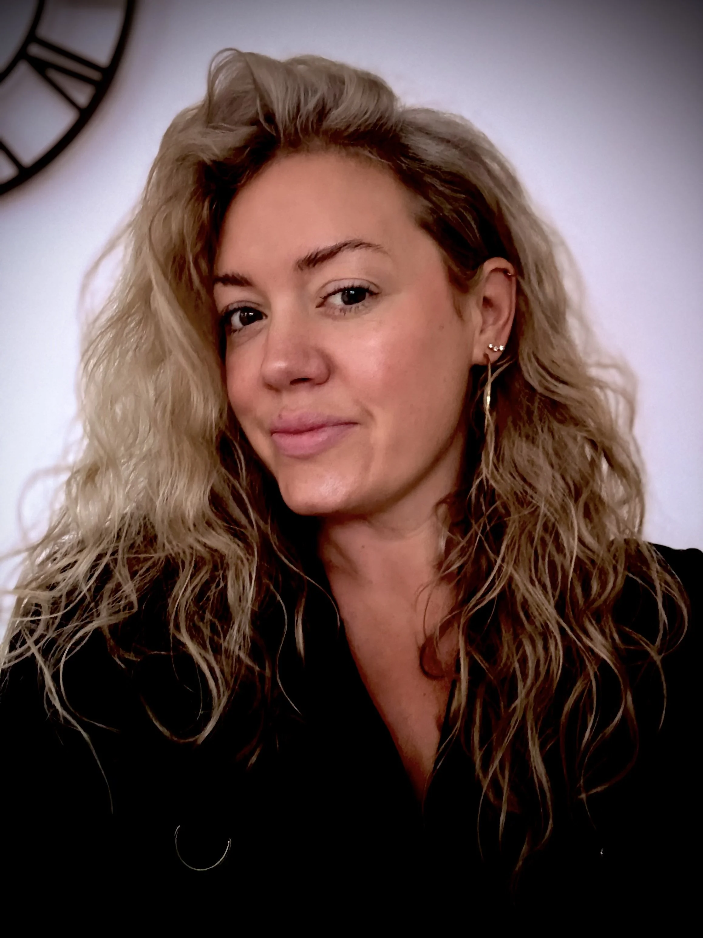 A woman with wavy blonde hair, smiling, wearing a black top.