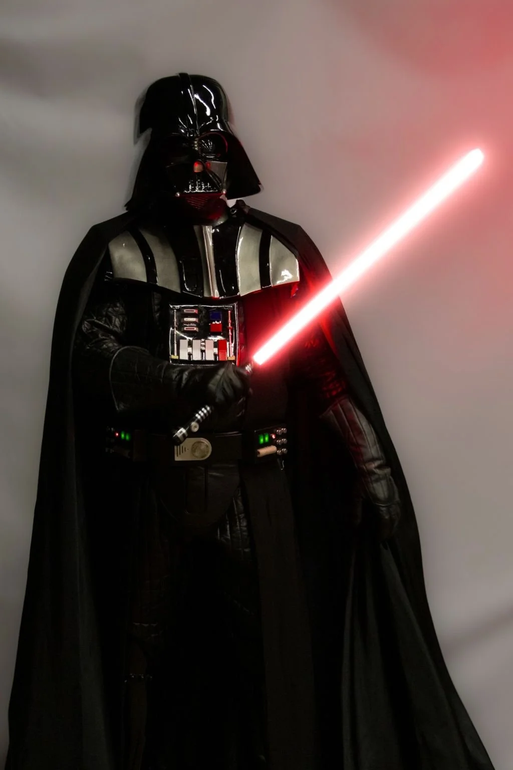 Darth Vader character with his black helmet, suit, cape, gloves, and a red lightsaber, standing against a plain background.