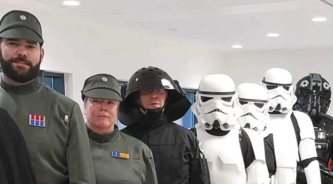 Group of people in Star Wars costumes including officers, a Stormtrooper, and a tie pilot, standing inside the childrens hospital.