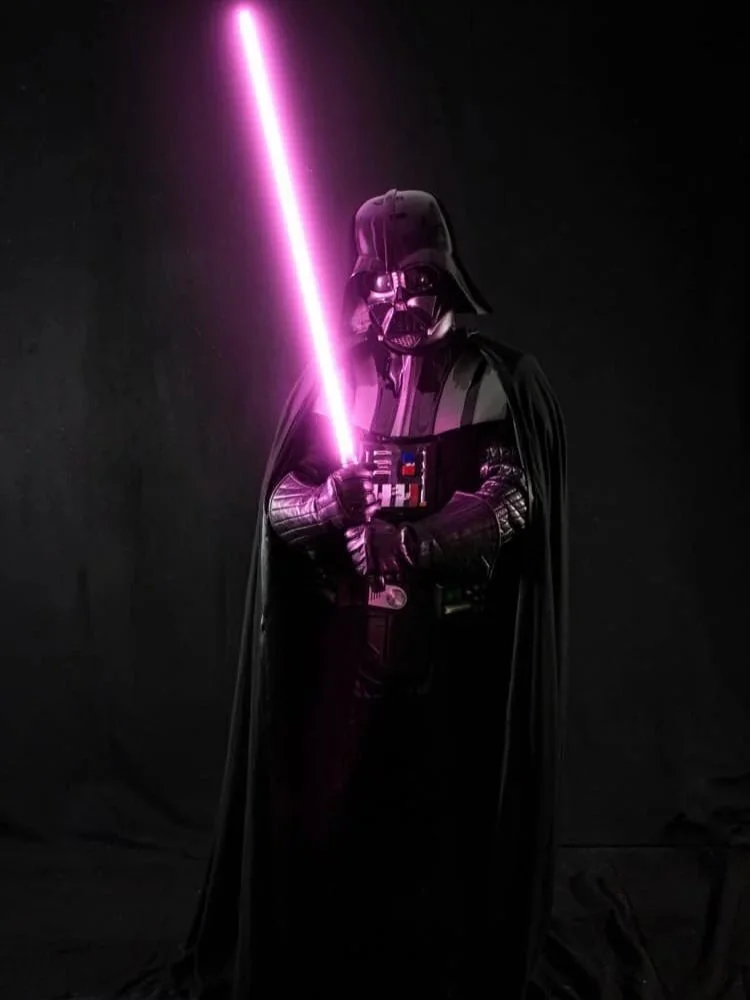 Darth Vader from Star Wars holding a glowing pink lightsaber against a dark background.