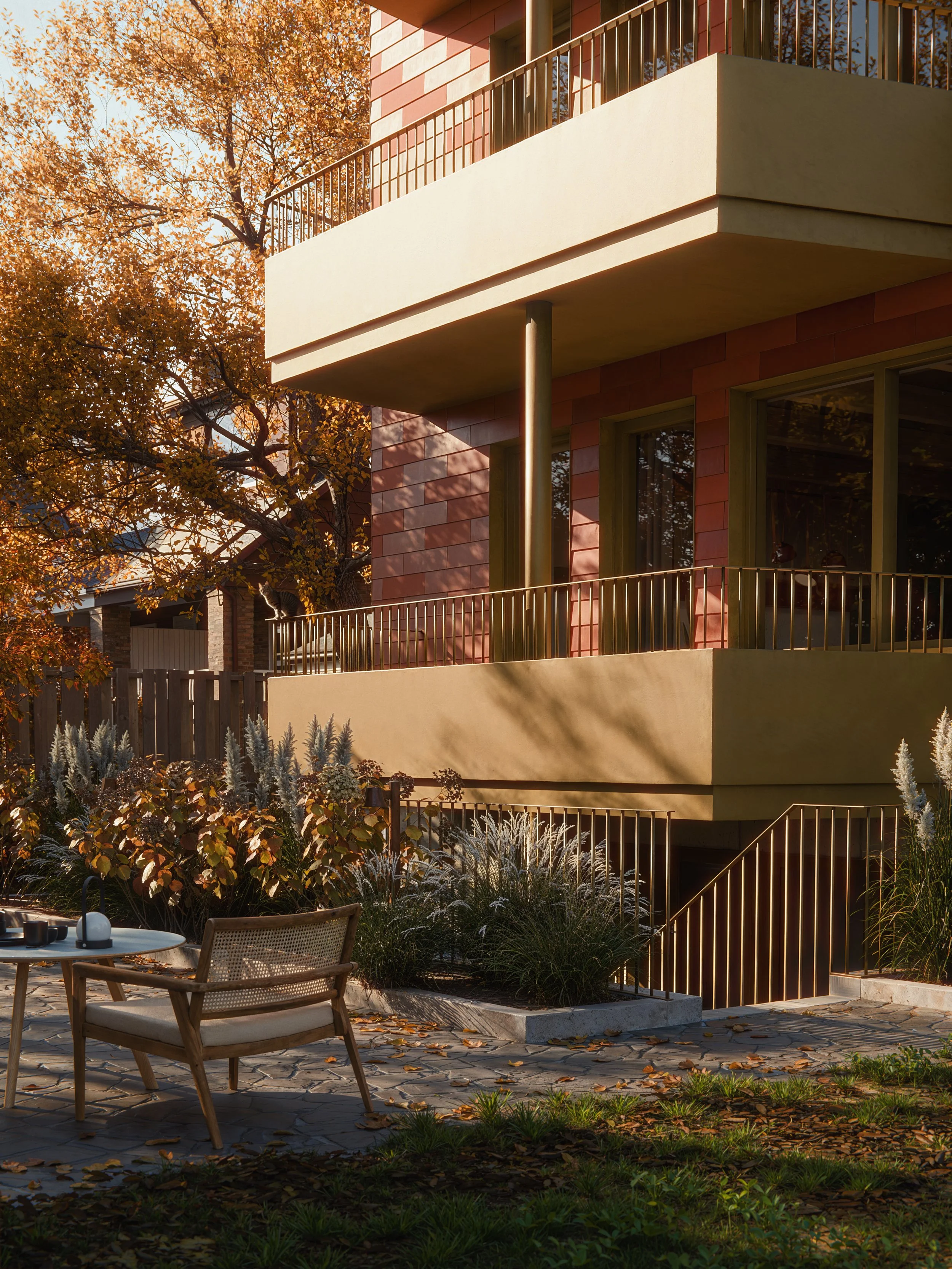 A modern multi-story residential building with balconies, surrounded by autumn foliage and landscaping, with outdoor furniture on stone-paved ground.