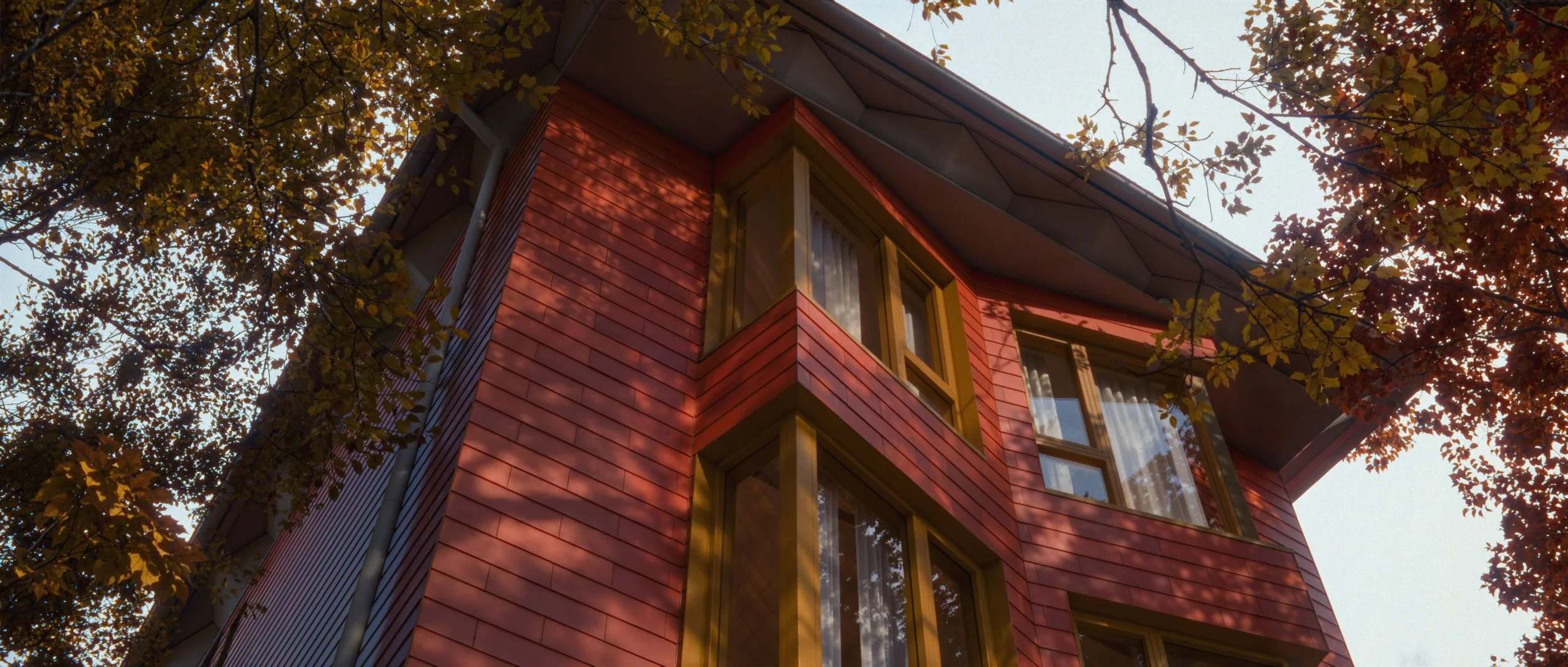 Red multi-story missing middle housing with large windows, surrounded by trees with autumn leaves, viewed from below.
