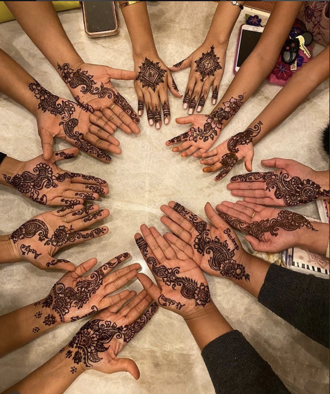 Multiple hands with intricate henna designs arranged in a circle on a table.