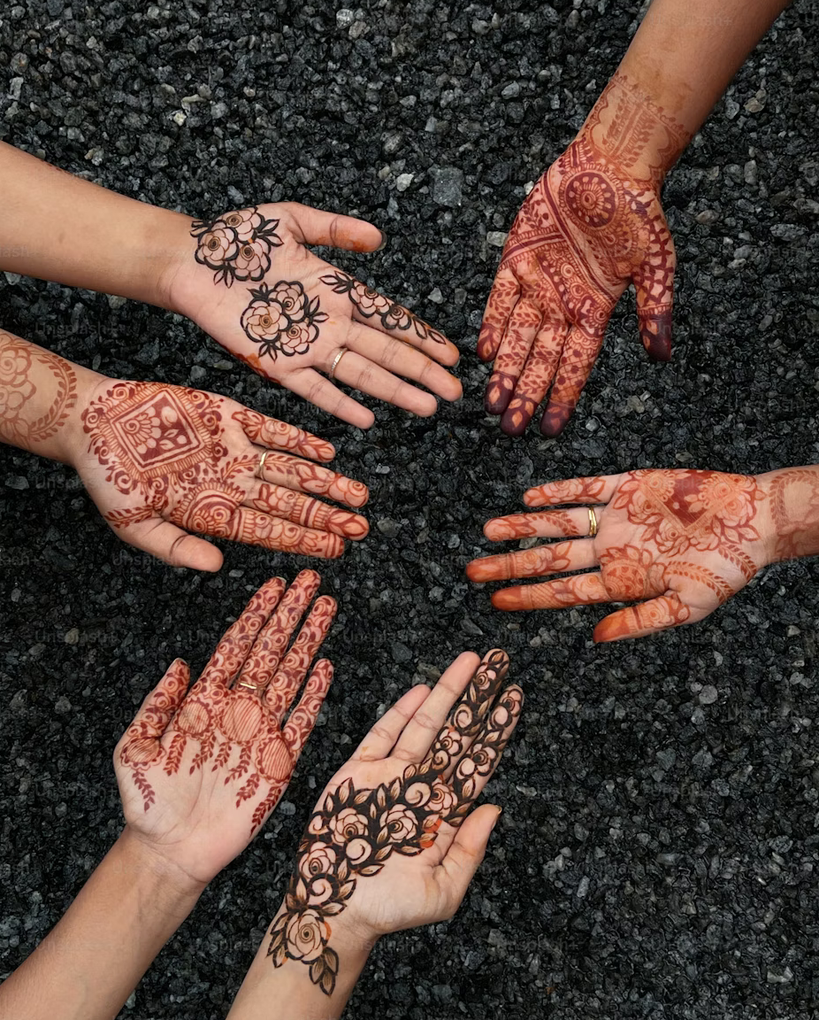 Six hands with intricate henna designs on the palms and fingers, arranged in a circle on a black textured surface.
