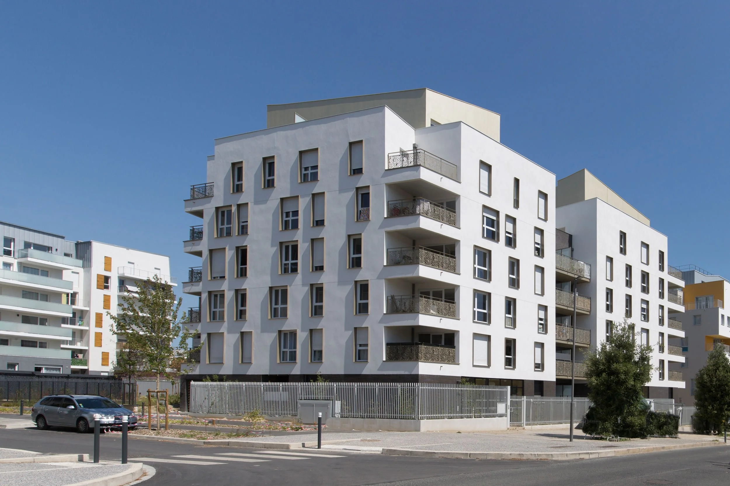 Bâtiment résidentiel moderne avec plusieurs étages, balcons, et fenêtres, sous un ciel bleu.