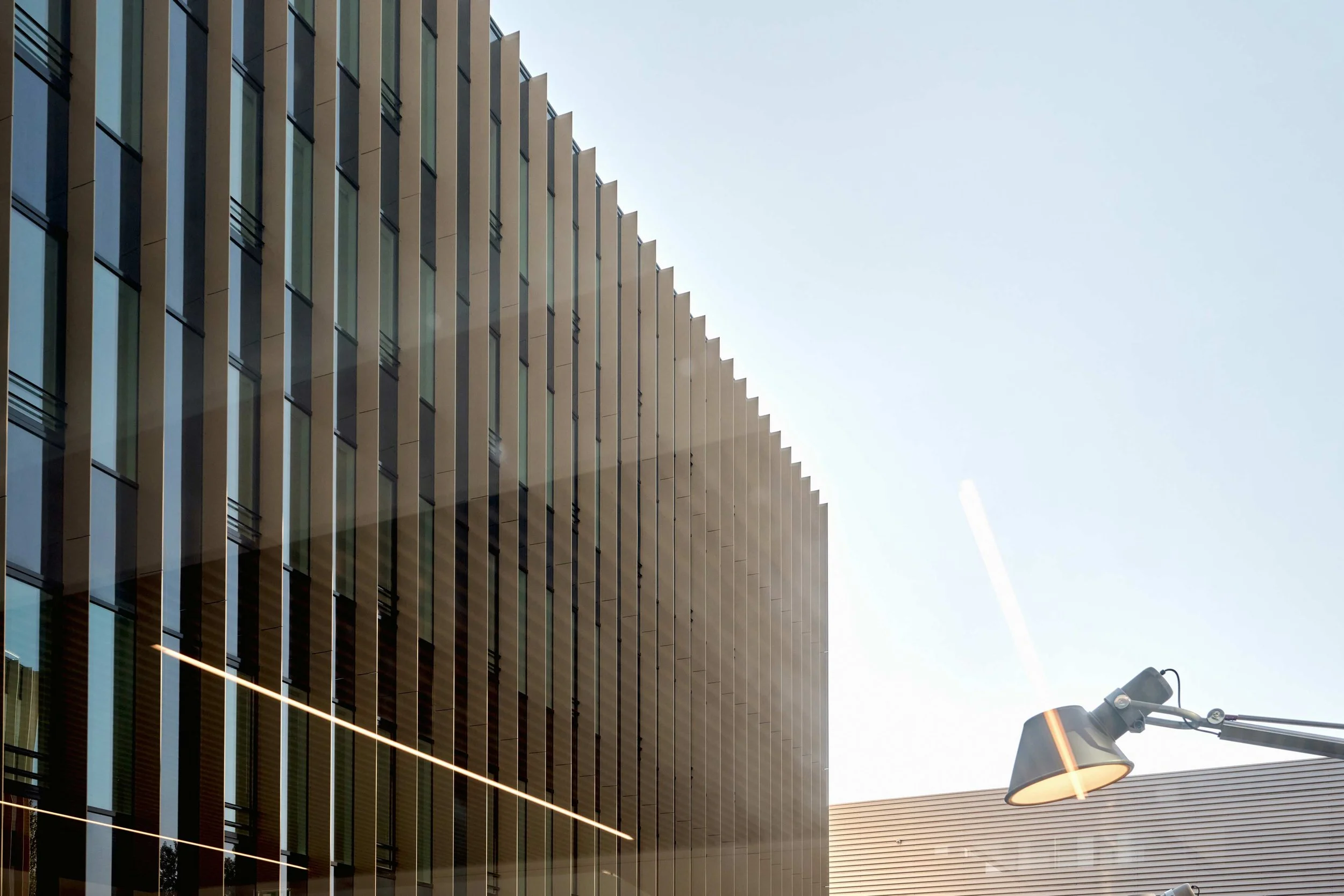 Facade moderne en verre avec de longues lignes lumineuses et un lampadaire urbain, ciel clair.