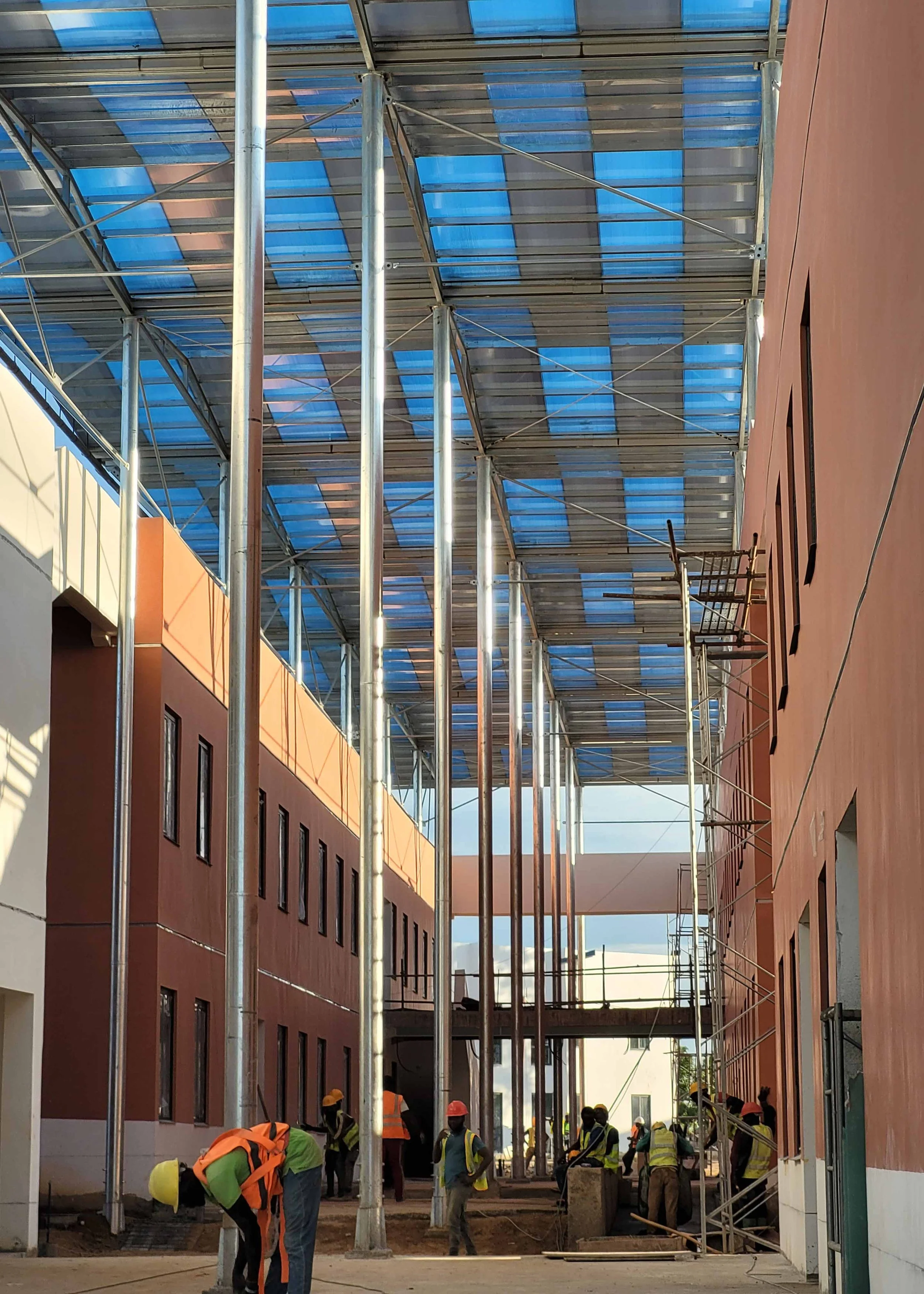 Travailleurs en sécurité construisant une structure avec des piliers métalliques entre deux bâtiments avec un toit en métal blue.