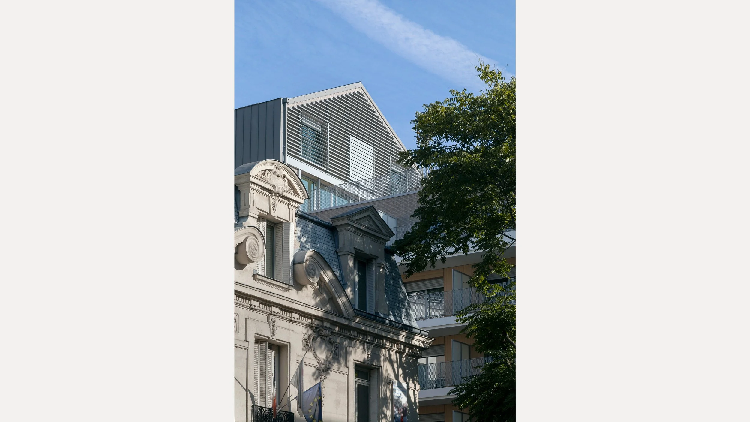Un vieux bâtiment en pierre avec des fenêtres à volets et des décorations ornementales, à côté d'un bâtiment moderne à plusieurs étages avec des balcons en verre et une façade en métal. Arbre avec des feuilles vertes à droite.