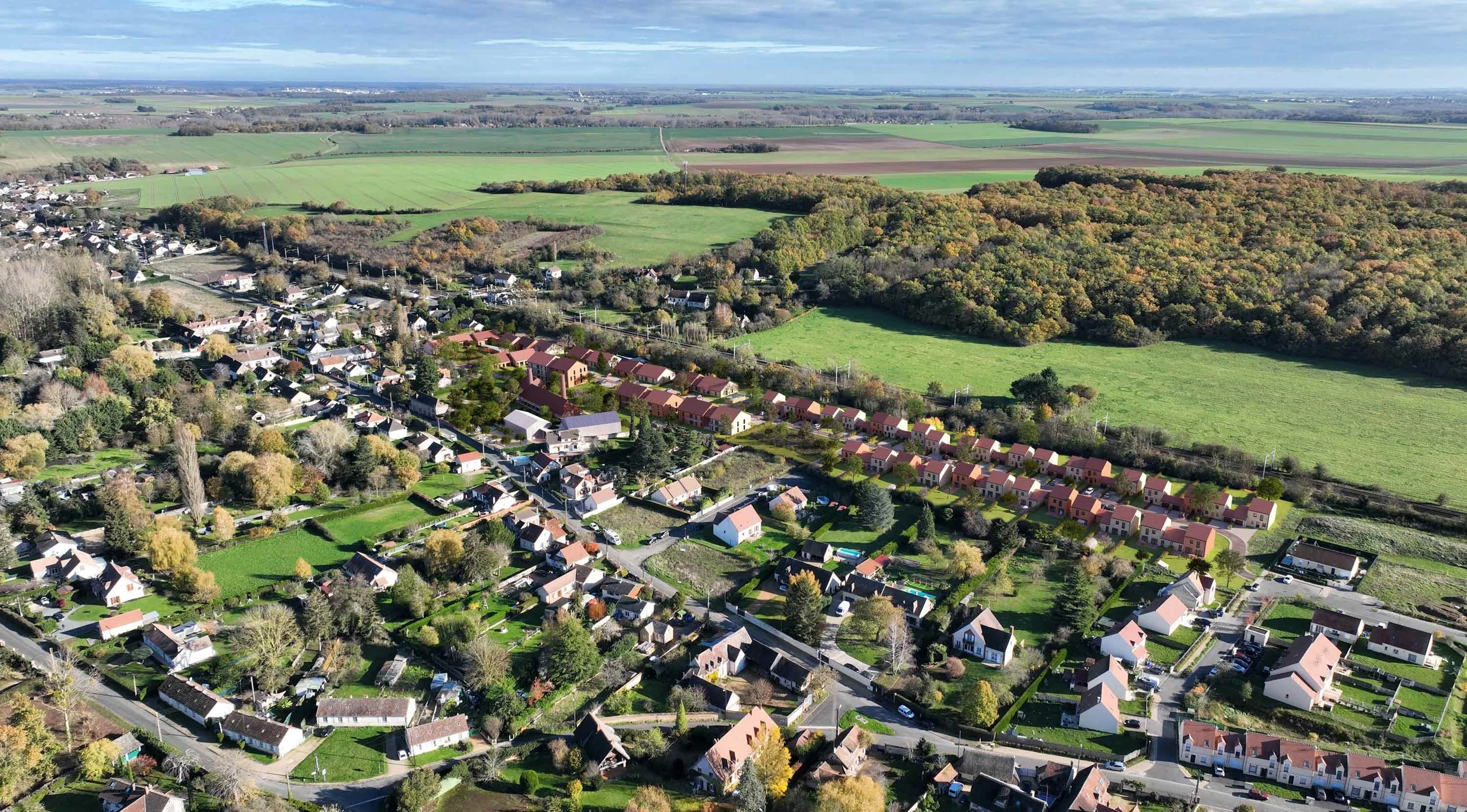 Vue aérienne d'un village résidentiel entouré de champs et de forêts en automne.