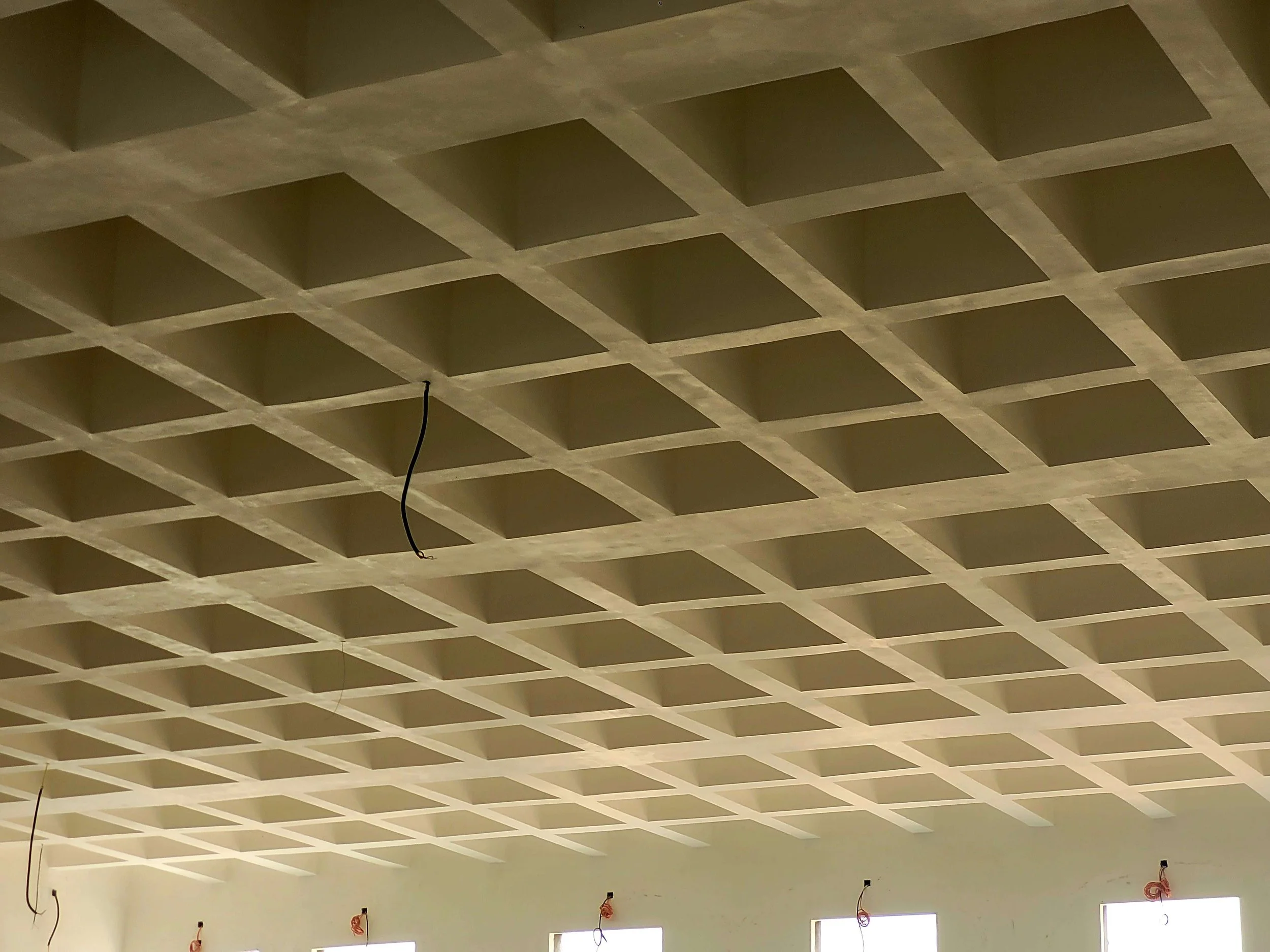 Plafond en béton avec des coffres carrés et un câble électrique suspendu.