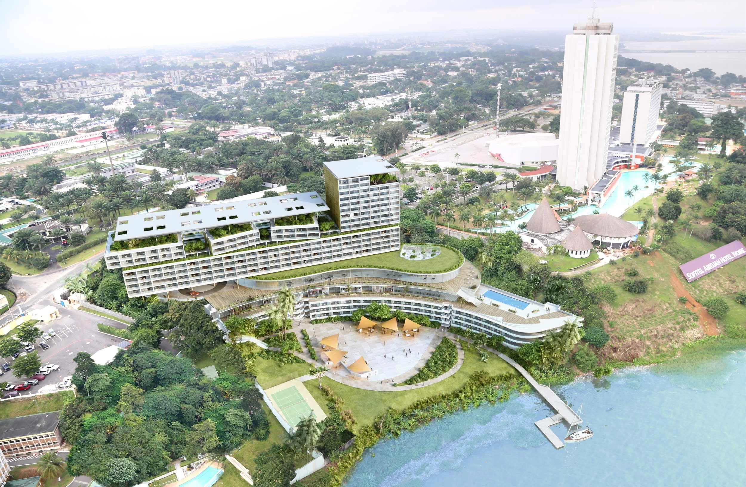 Vue aérienne d'un complexe hôtelier moderne avec bâtiments blancs, une piscine, un espace de détente avec parasols, un court de tennis, et un accès à une plage à proximité.