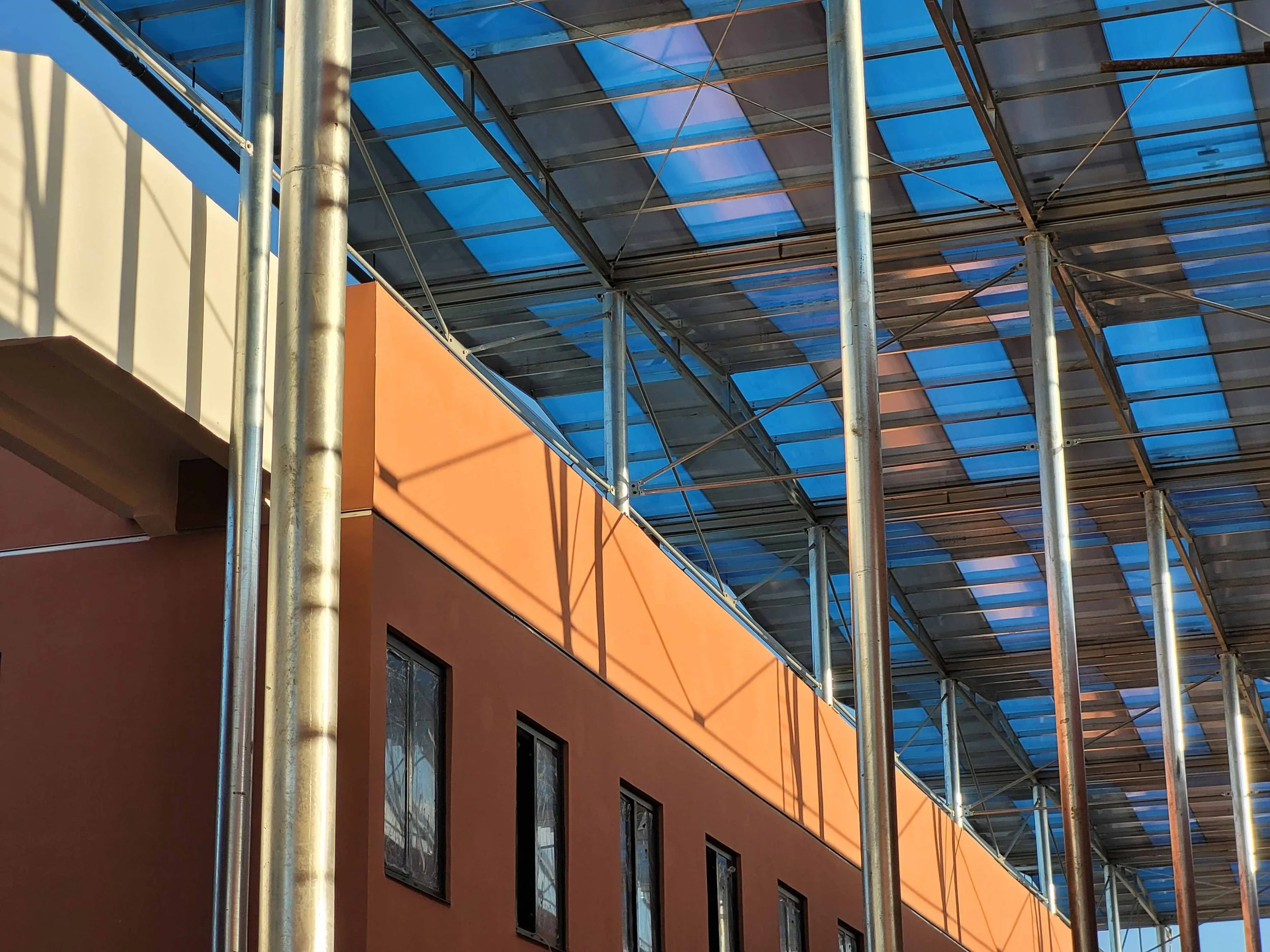 Une structure métallique avec un toit en panneaux bleus au-dessus d'un bâtiment orange avec plusieurs fenêtres.