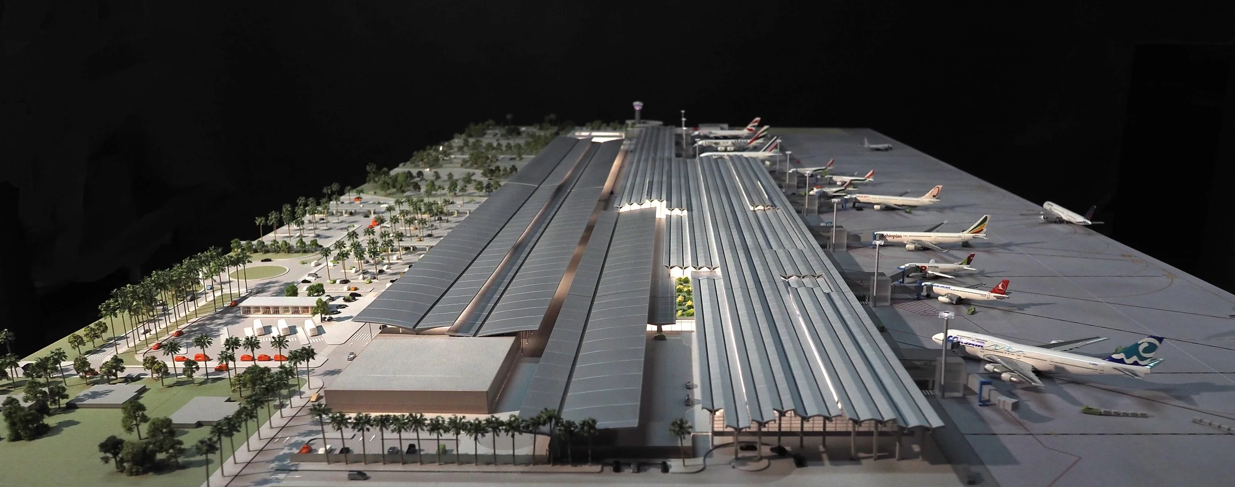 Modèle réduit d'un aéroport avec terminaux et avions au sol, entouré d'arbres et de parkings.