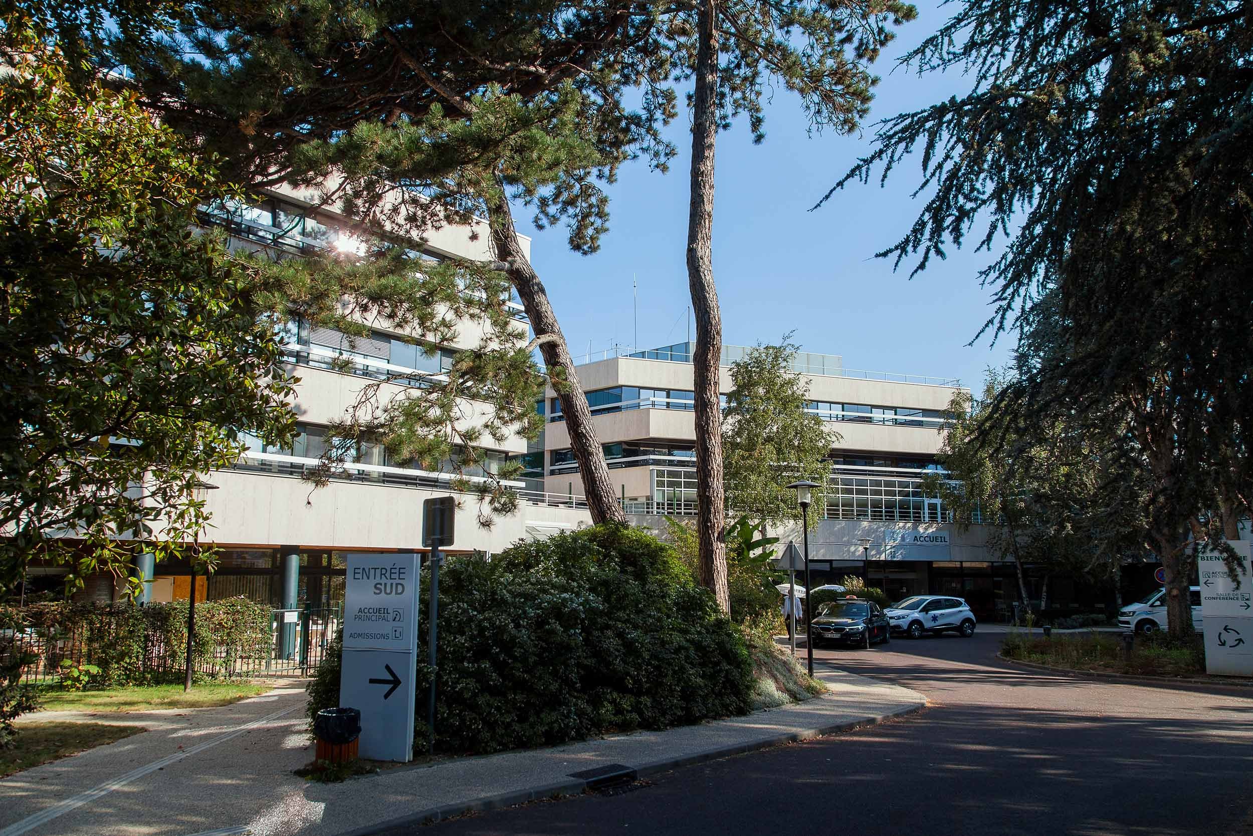 Bâtiment moderne avec plusieurs étages, entouré d'arbres et de véhicules, avec un panneau indiquant l'entrée sud.