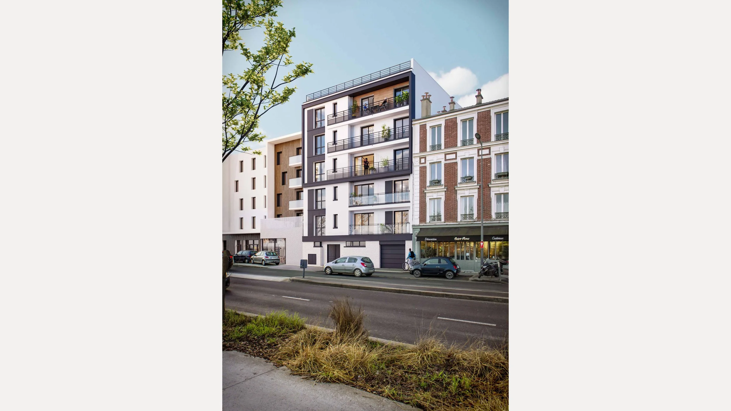 Immeuble moderne à plusieurs étages avec balcons noirs, situé entre des bâtiments anciens en briques. Voitures garées devant, personne à vélo et à pied, arbre en premier plan, sky bleu avec quelques nuages.