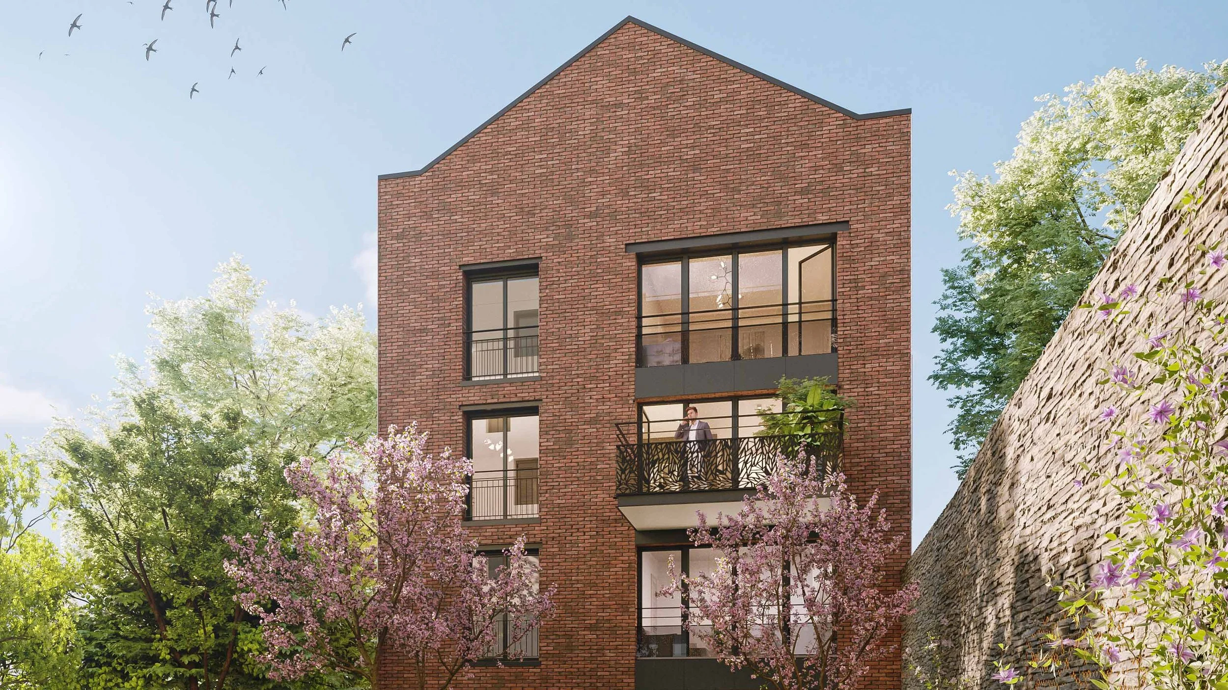 Un bâtiment en briques rouges avec des fenêtres modernes, entouré d'arbres en fleurs roses et verts, sous un ciel bleu avec quelques oiseaux envolés.