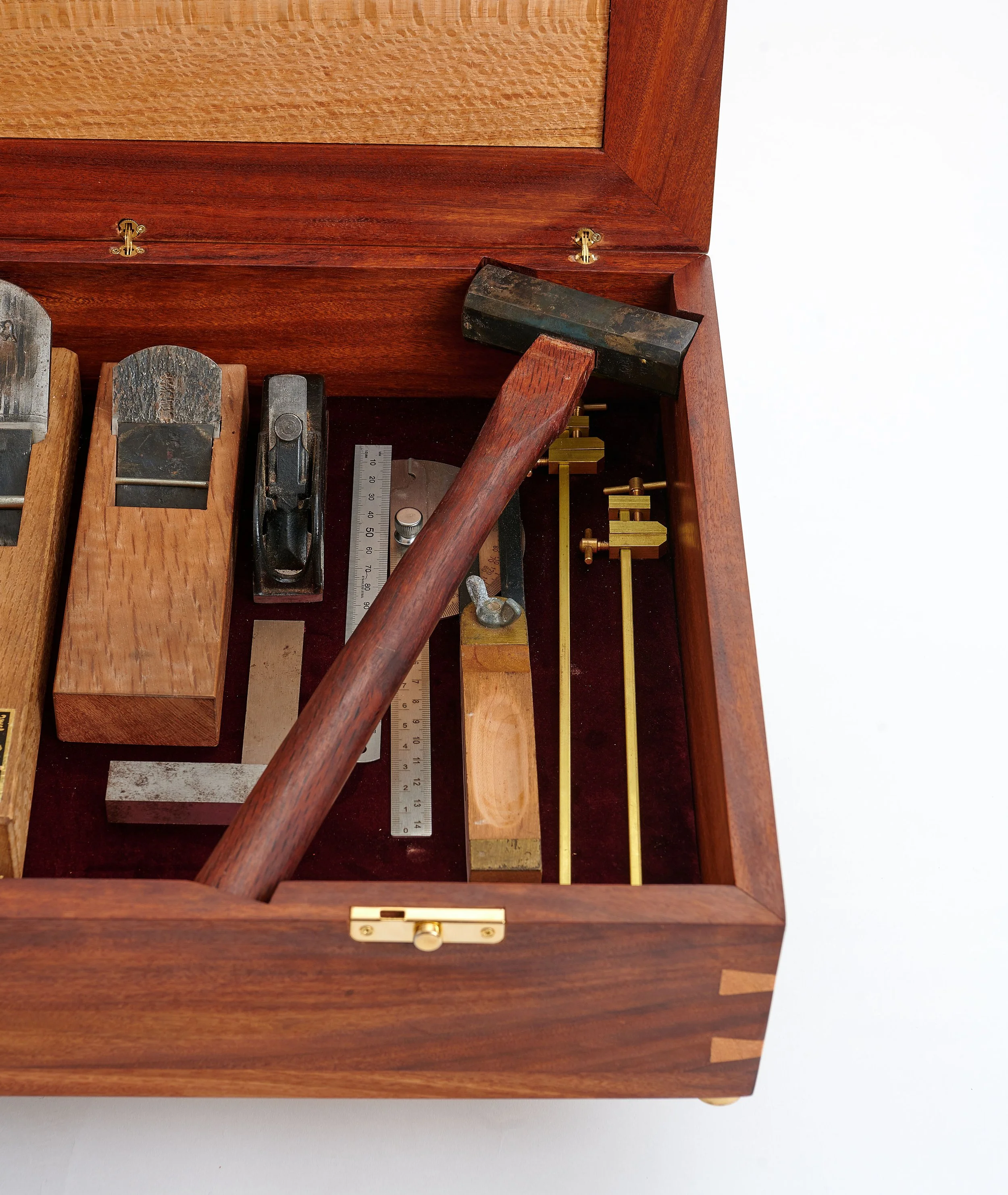 Top view of a wooden toolbox with a hammer inside, a ruler, a square, and small brass clamps.