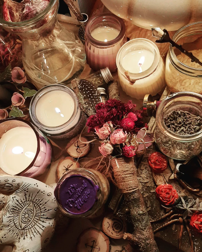 A collection of lit candles in glass jars, dried flowers, wooden slices with symbols, and various decorative items on a wooden surface.