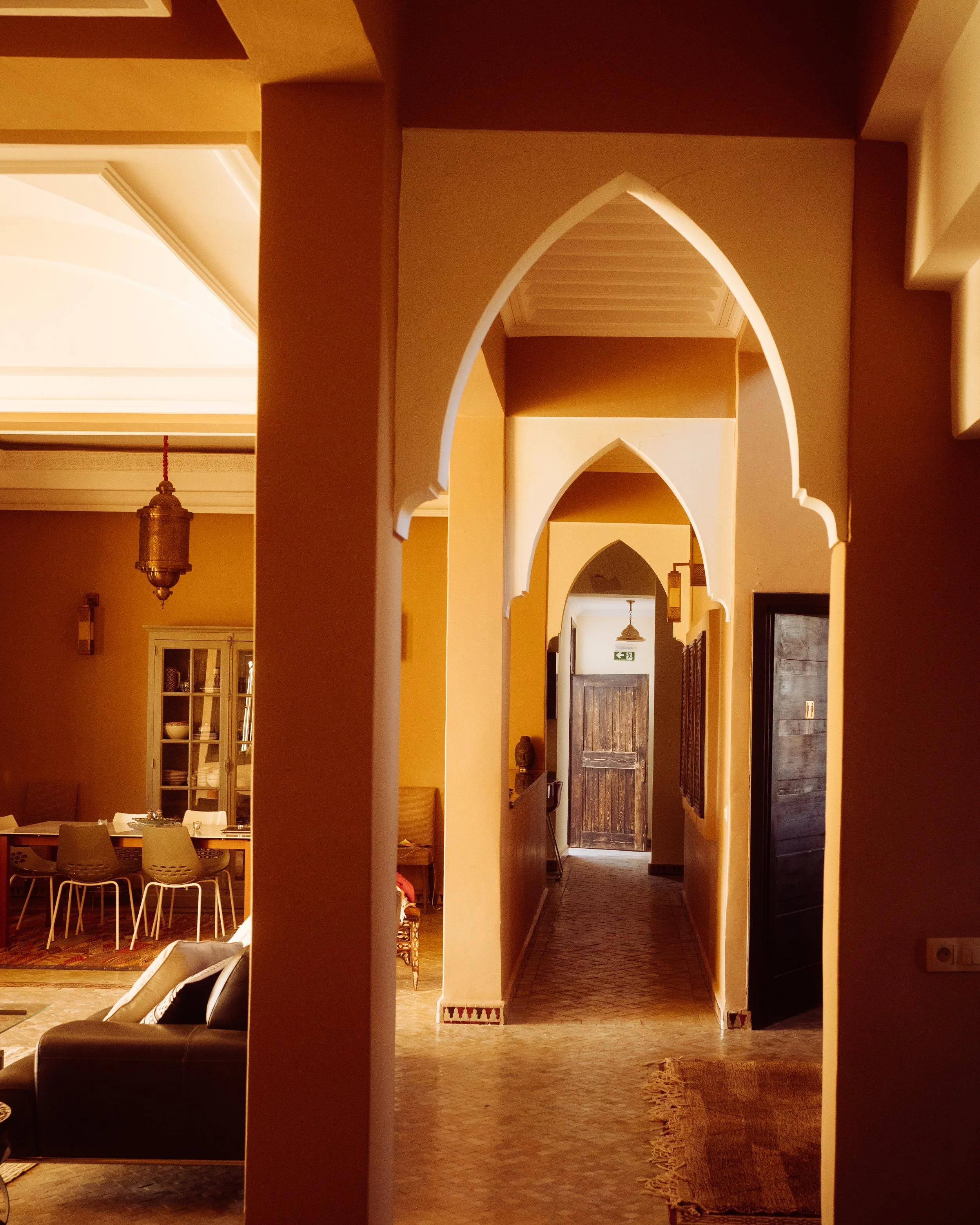 Interior view of a house with a hallway and archways, warm lighting, a dining table with chairs, and decorative items, featuring a mix of traditional and contemporary decor.