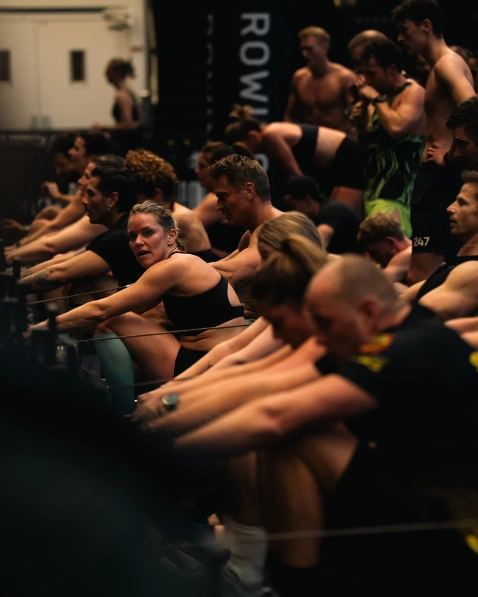 People participating in a rowing competition or training session, sitting on indoor rowing machines.