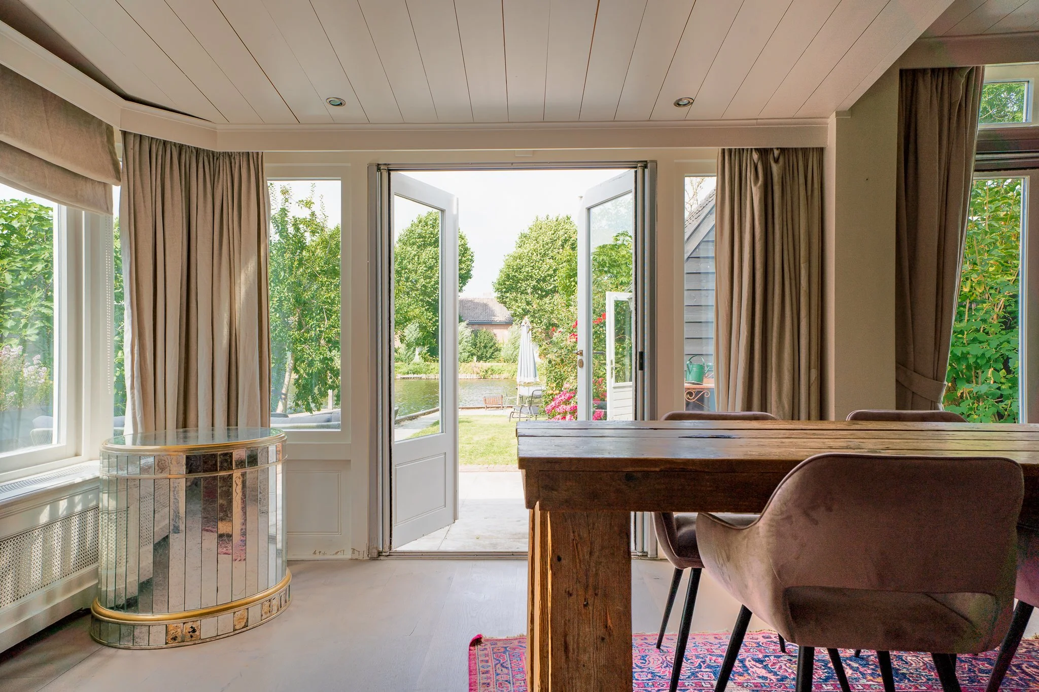 View through open patio doors showing a backyard garden with trees, flowers, and outdoor furniture.