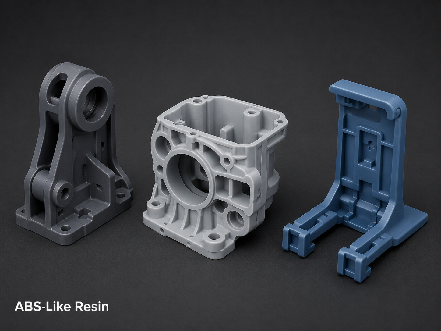 Three 3D printed parts of different shapes and colors on a black background. The first is gray with multiple holes and a round opening; the second is white with a central circular opening and various structural details; the third is blue with a rectangular shape and multiple compartments. Label in bottom left corner says "ABS-Like Resin."